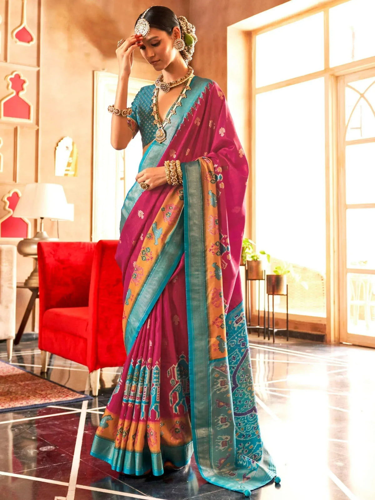 Woman in vibrant pink and teal designer saree with elephant print, traditional jewelry, and floral hair accessory