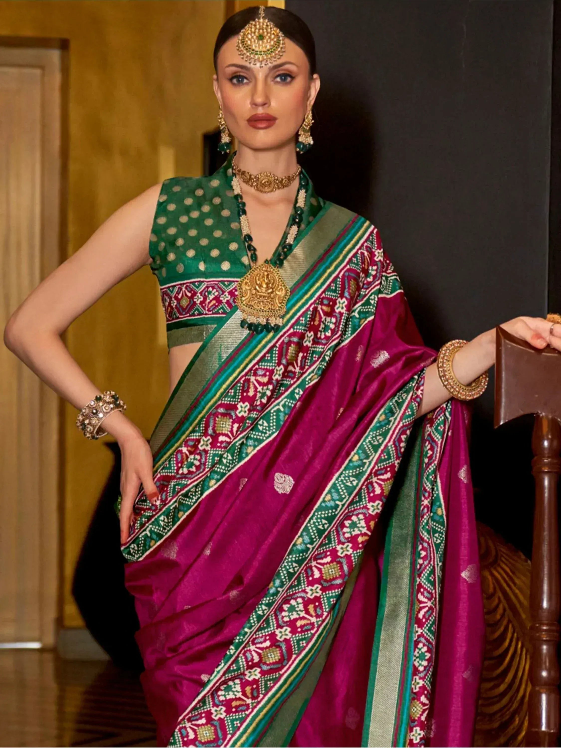 Woman in vibrant magenta and green embroidered saree with gold jewelry, traditional Indian ethnic wear
