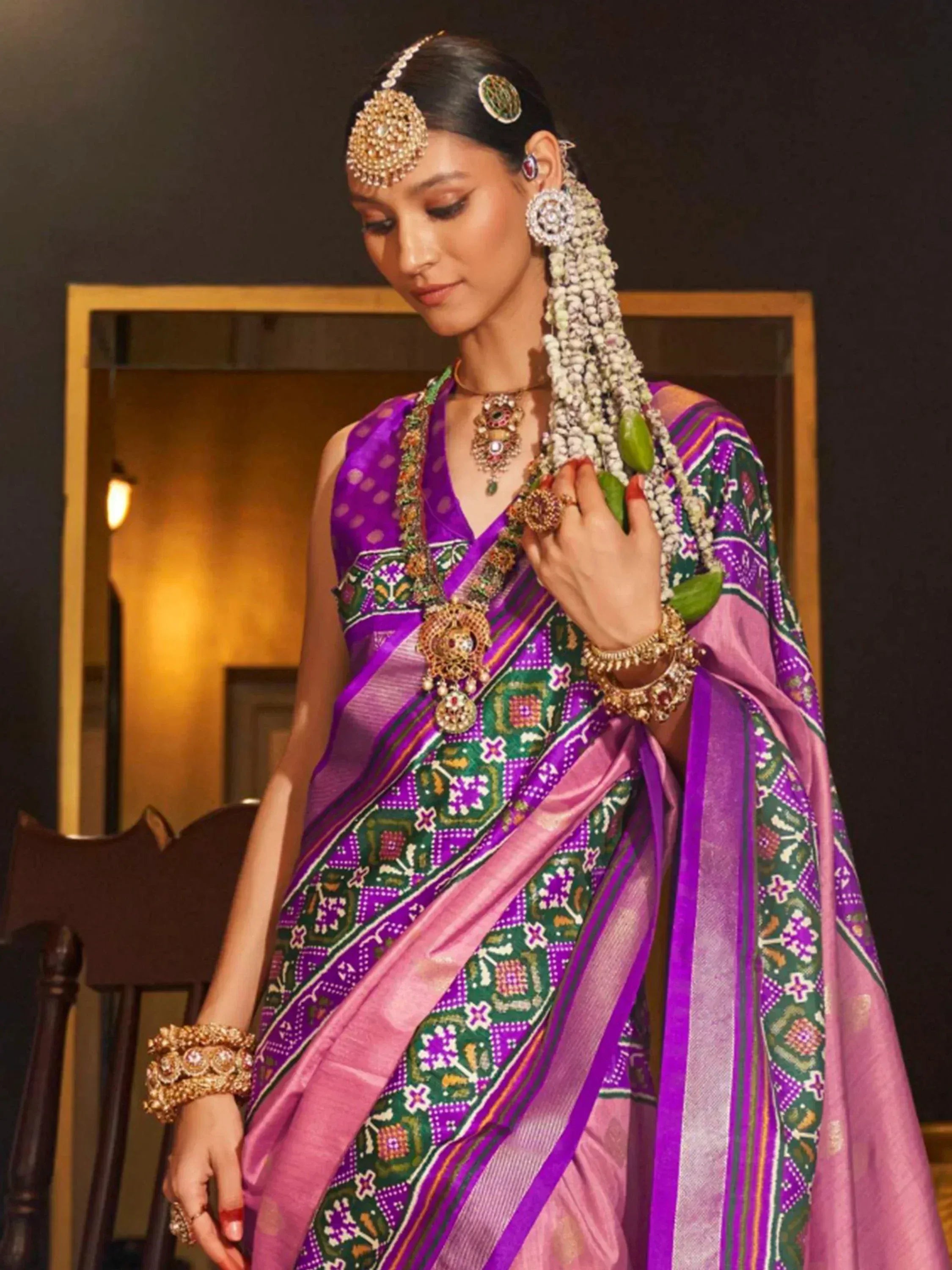 Woman in vibrant purple and green ethnic saree with intricate embroidery and traditional jewelry