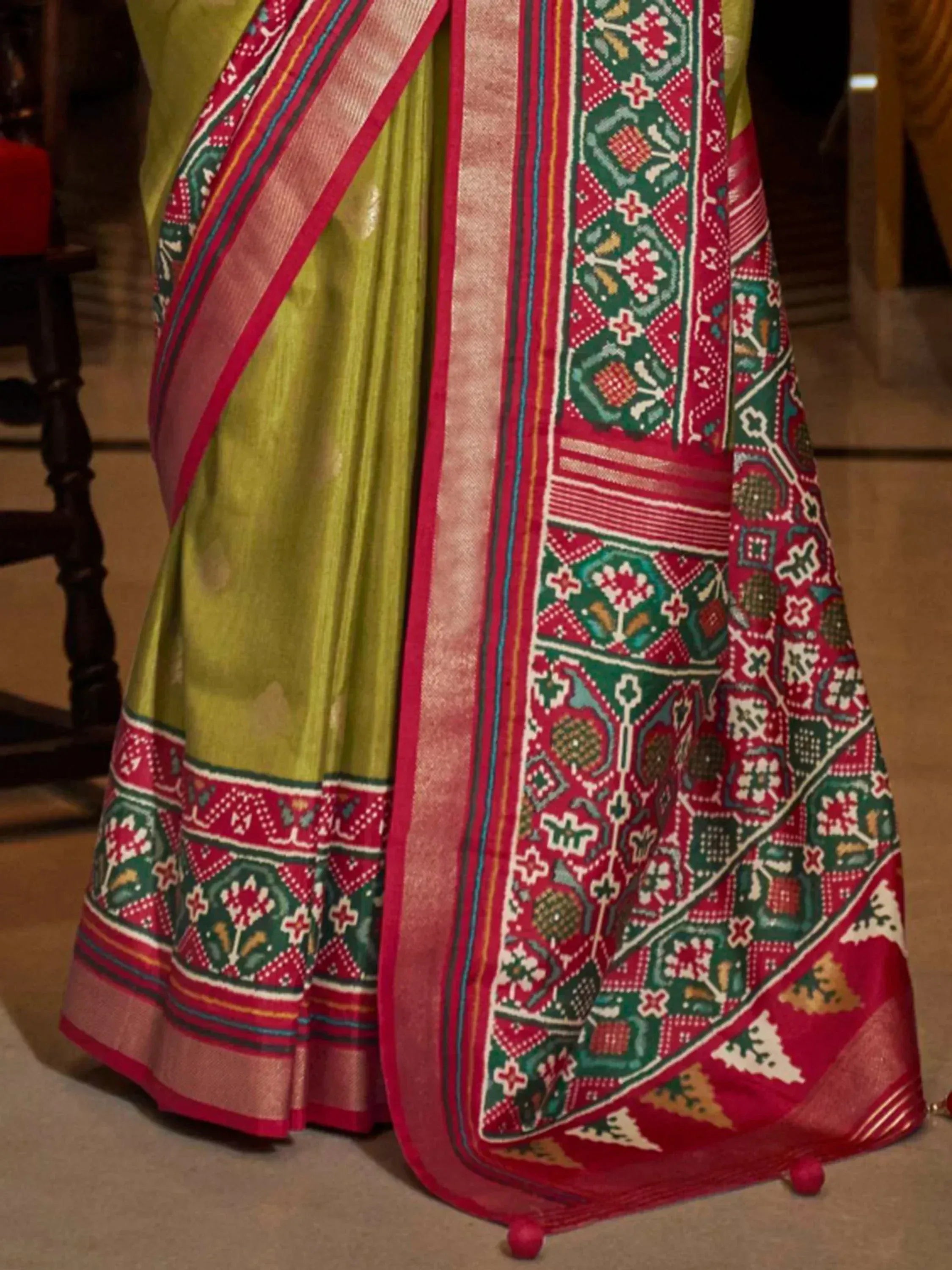 Green and red ethnic saree with intricate geometric and floral border patterns, perfect for festive occasions.