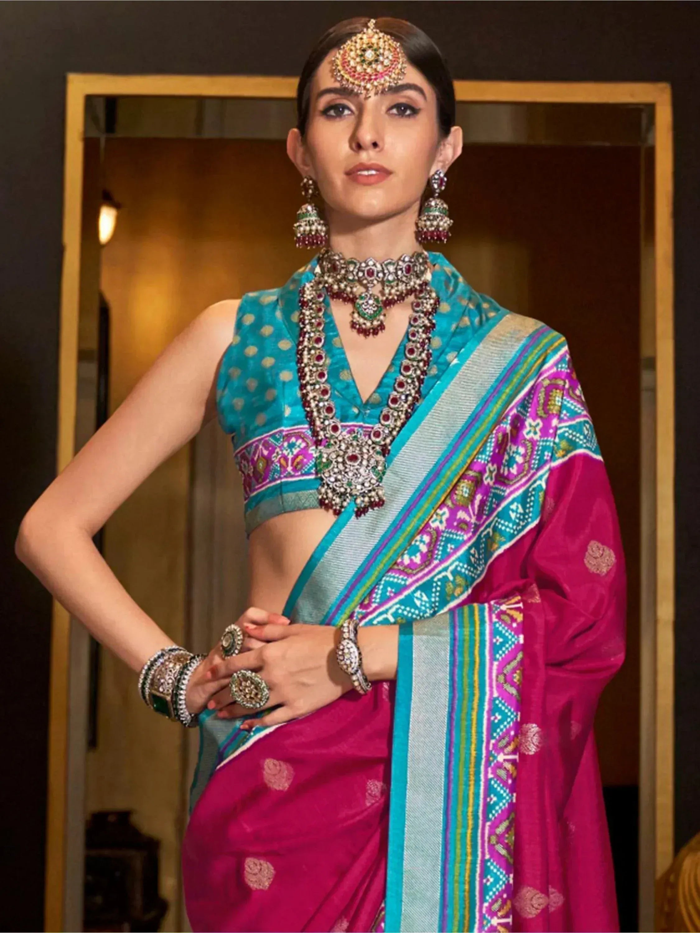Woman in vibrant pink and teal ethnic saree with intricate jewelry, perfect for Indian celebrations.