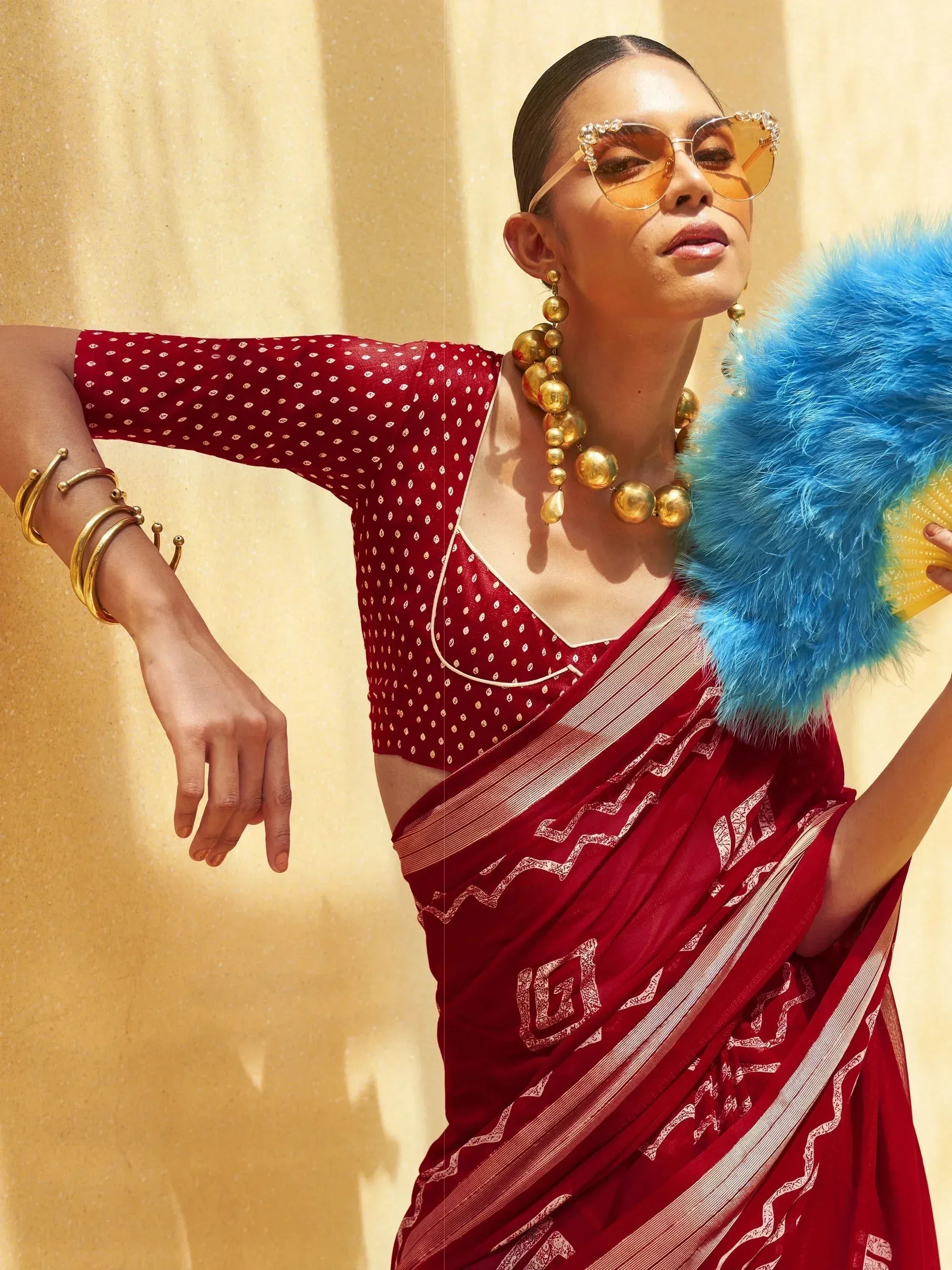Red printed saree with gold jewelry and blue feather fan, stylish ethnic wear for women