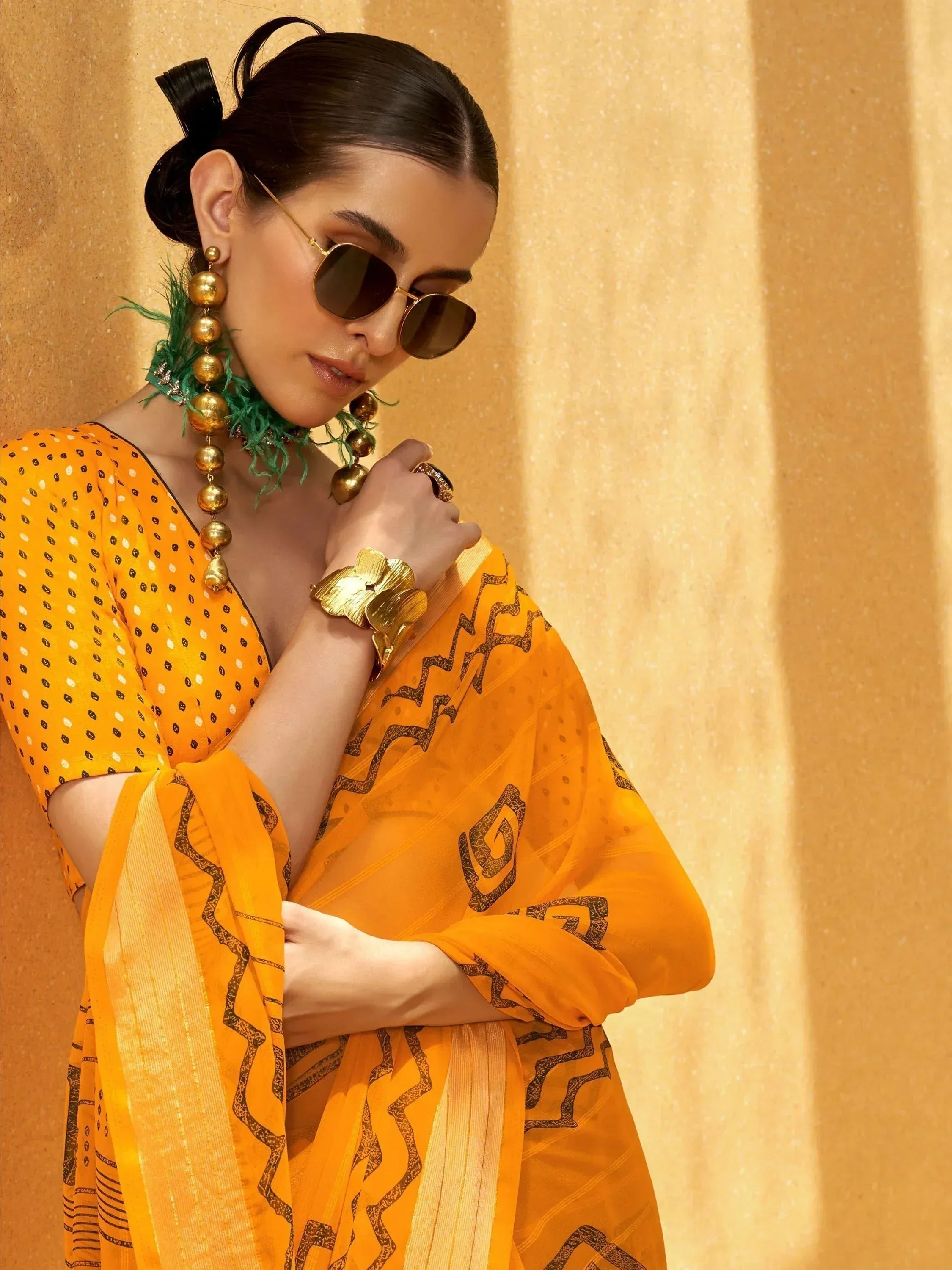 Woman in vibrant yellow printed saree with gold jewelry and sunglasses, ethnic Indian wear