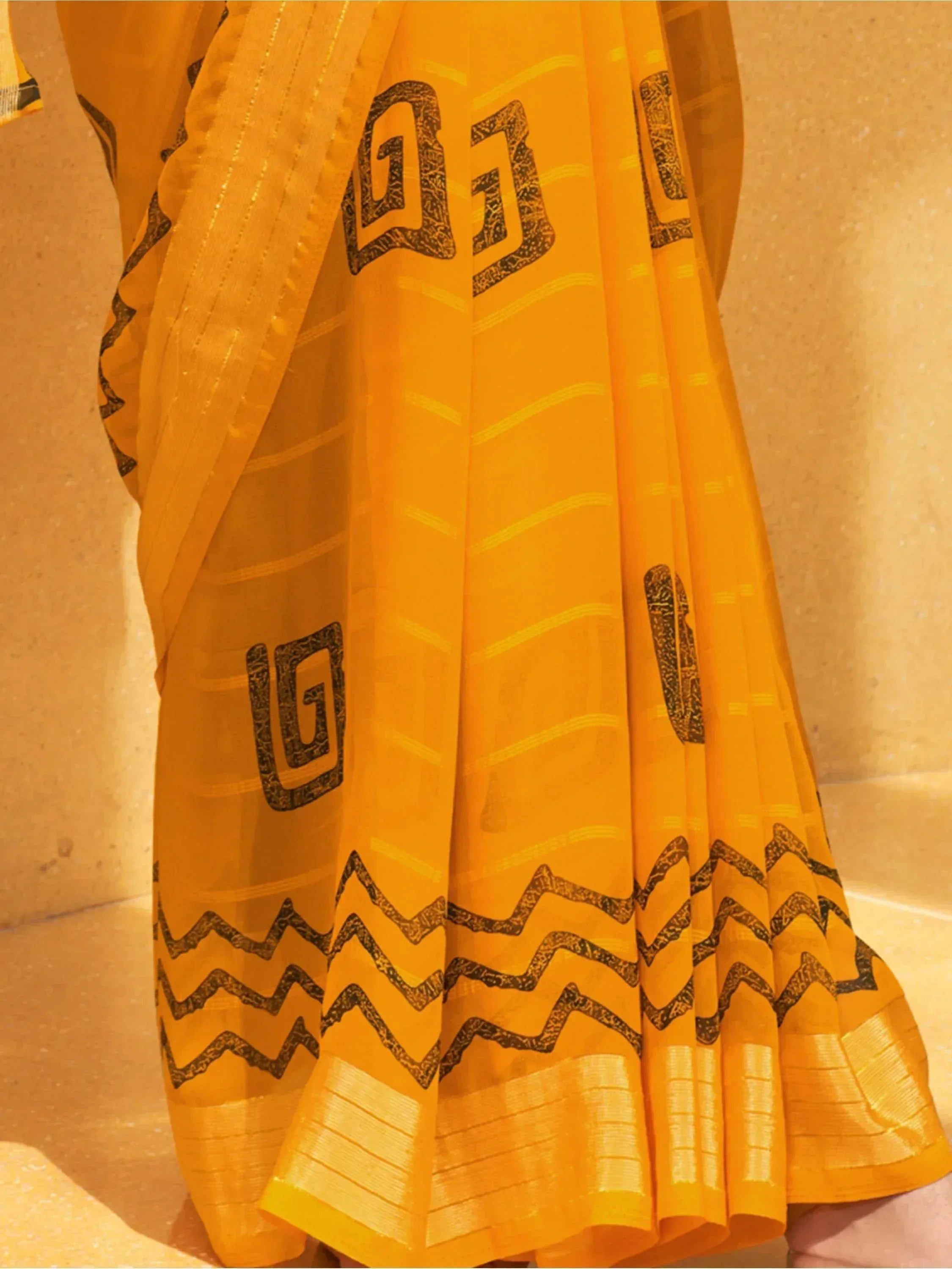 Vibrant yellow saree with black geometric print and gold border, ethnic Indian wear