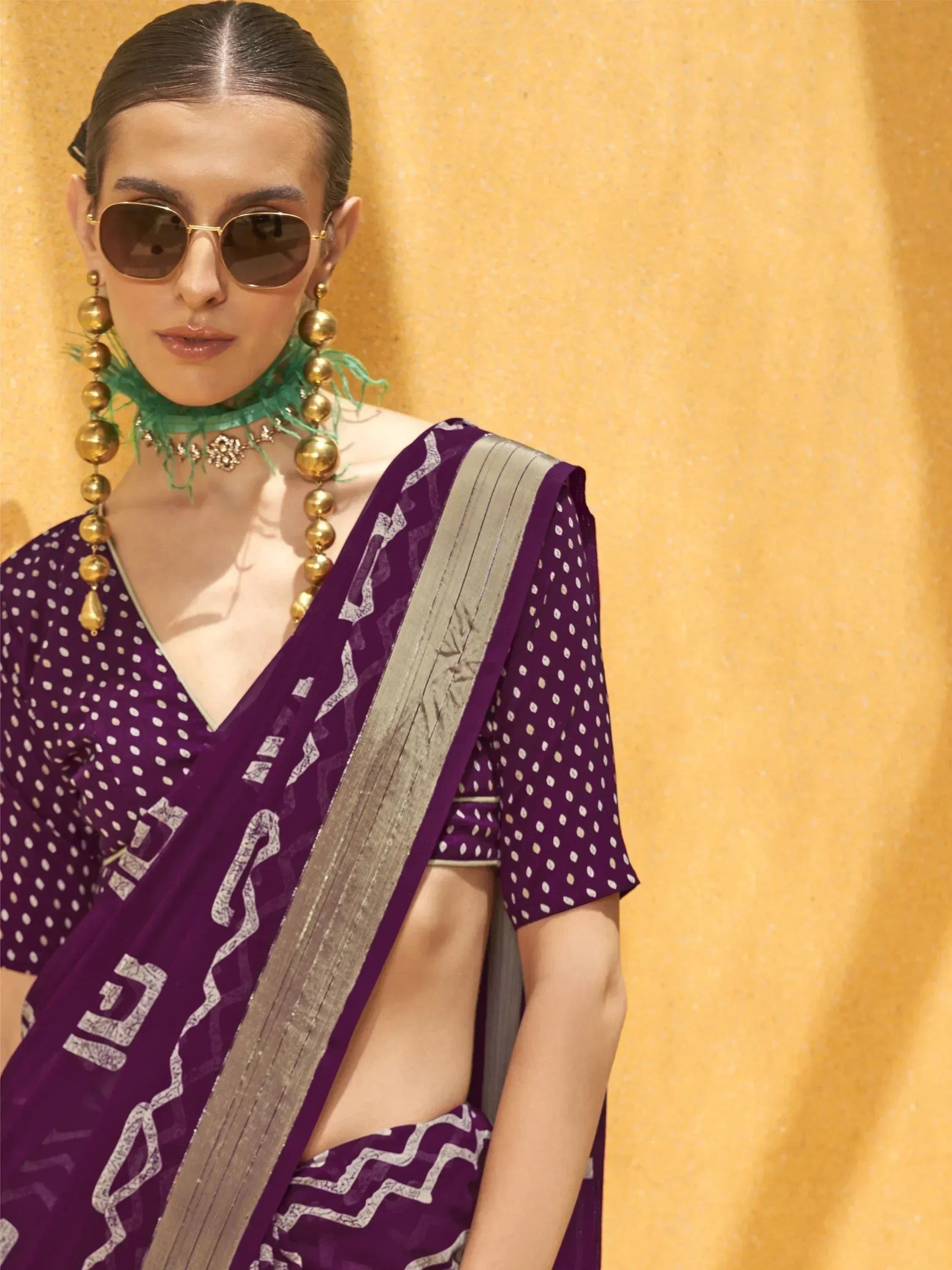 Purple printed saree with silver border, paired with statement gold earrings and sunglasses, styled for modern ethnic fashion.