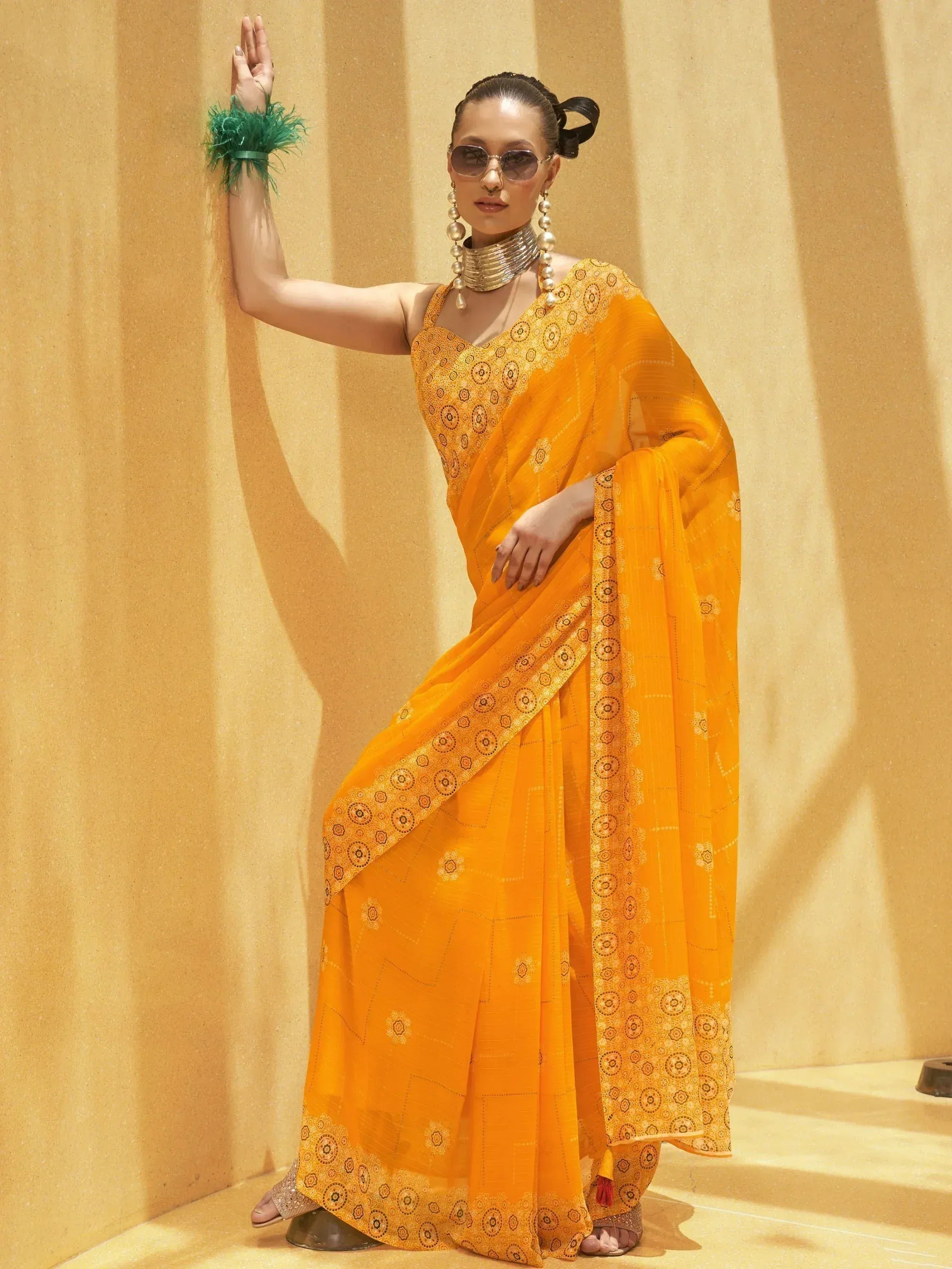 Vibrant yellow printed saree with ethnic motifs, styled with statement jewelry and sunglasses for festive occasions.