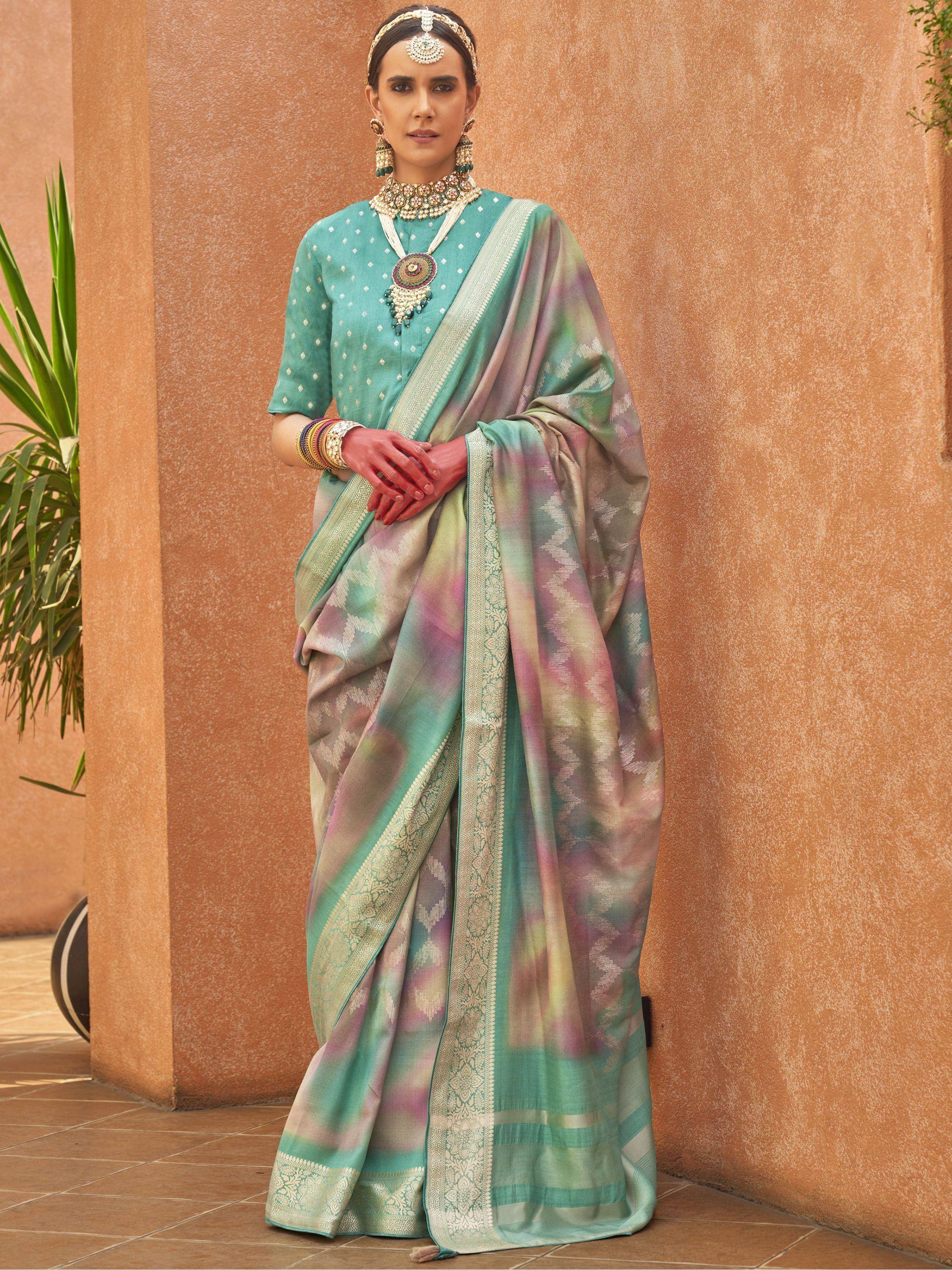 Woman in teal designer saree with pastel ombre pallu and gold border, paired with traditional jewelry