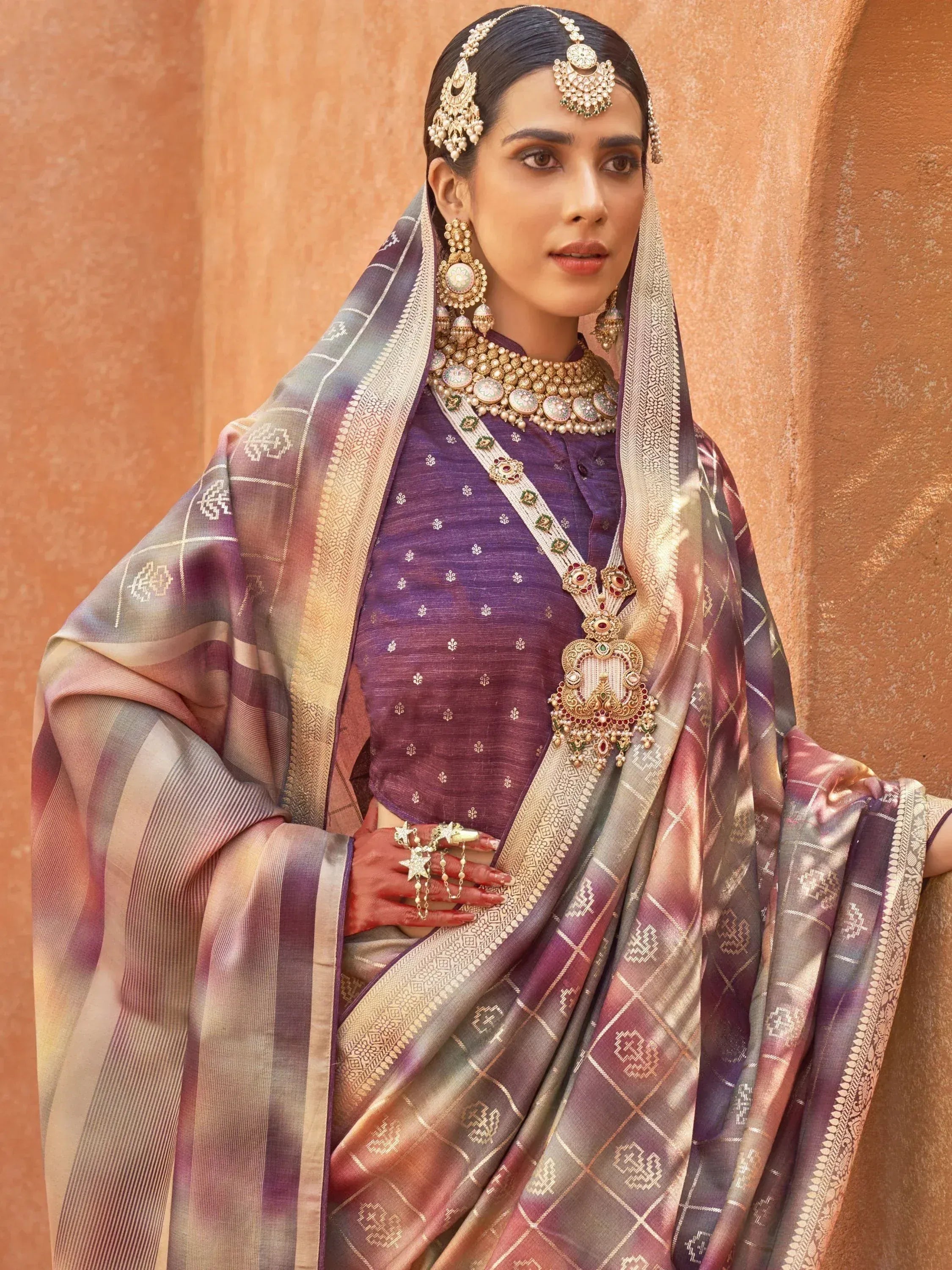 Woman in purple ethnic saree with gold jewelry and traditional headpiece, perfect for Indian weddings or festive occasions.