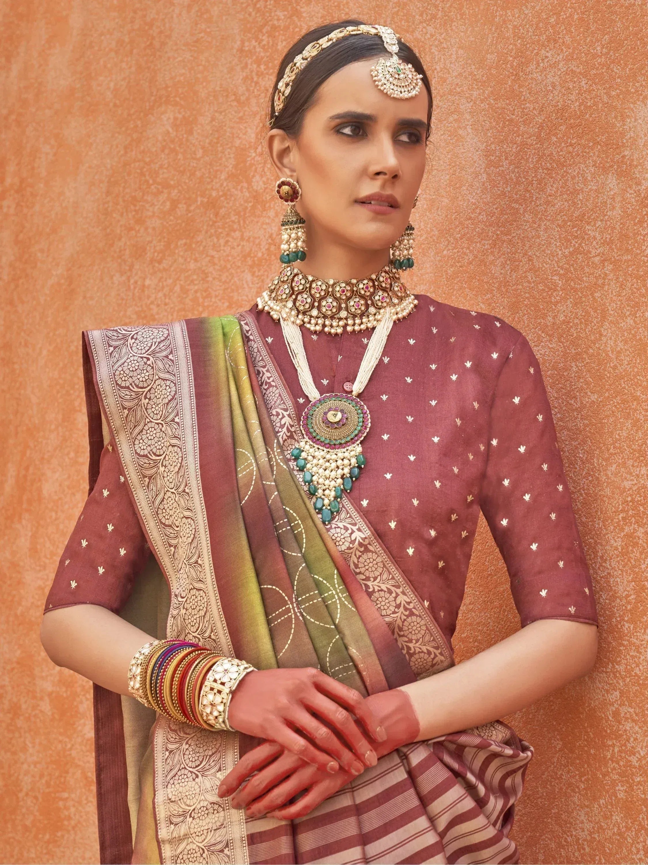 Woman in maroon ethnic saree with gold embroidery, traditional jewelry, and floral blouse for festive occasions