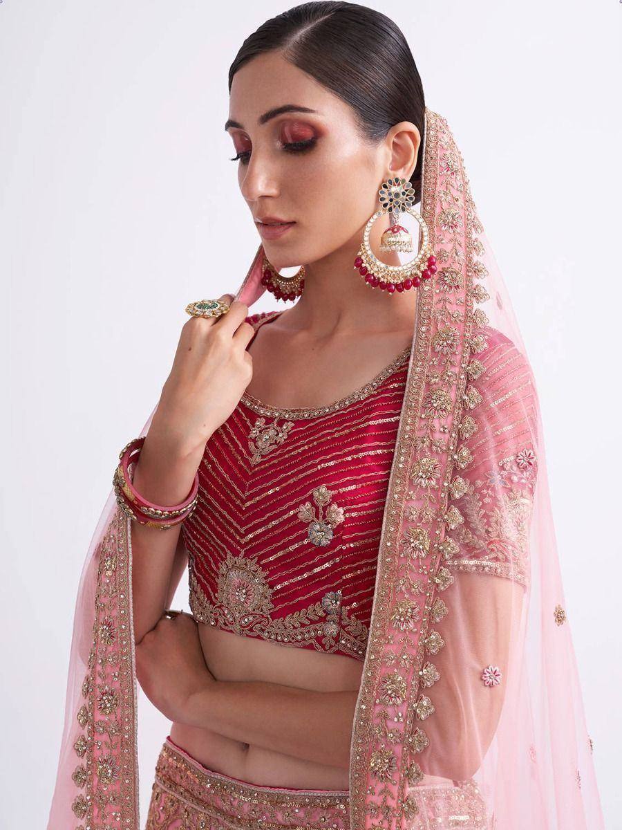 Red and pink embroidered lehenga choli with gold detailing and matching dupatta, styled with jhumka earrings.