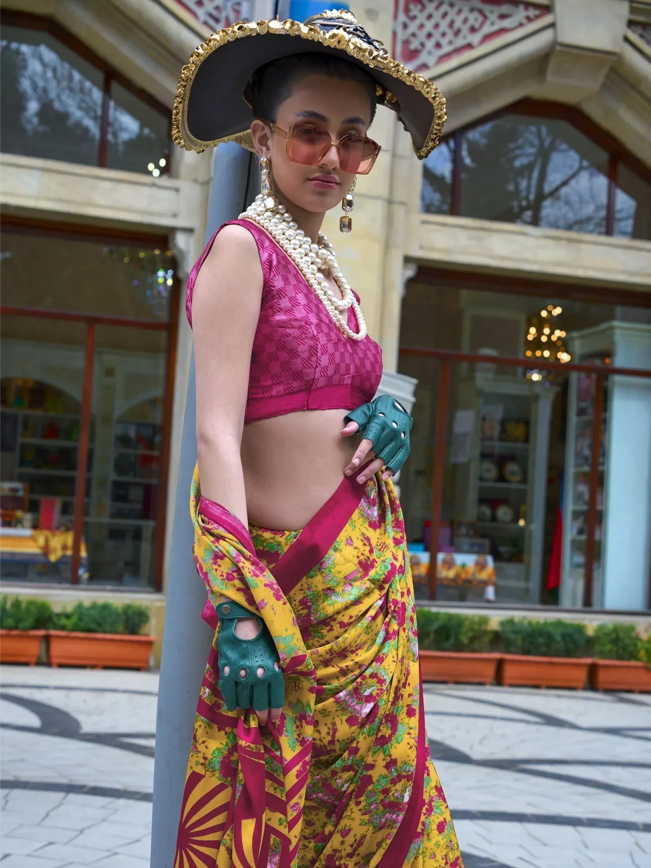 Woman in vibrant floral saree with pink blouse, gold hat, and pearl jewelry, styled for ethnic fashion.