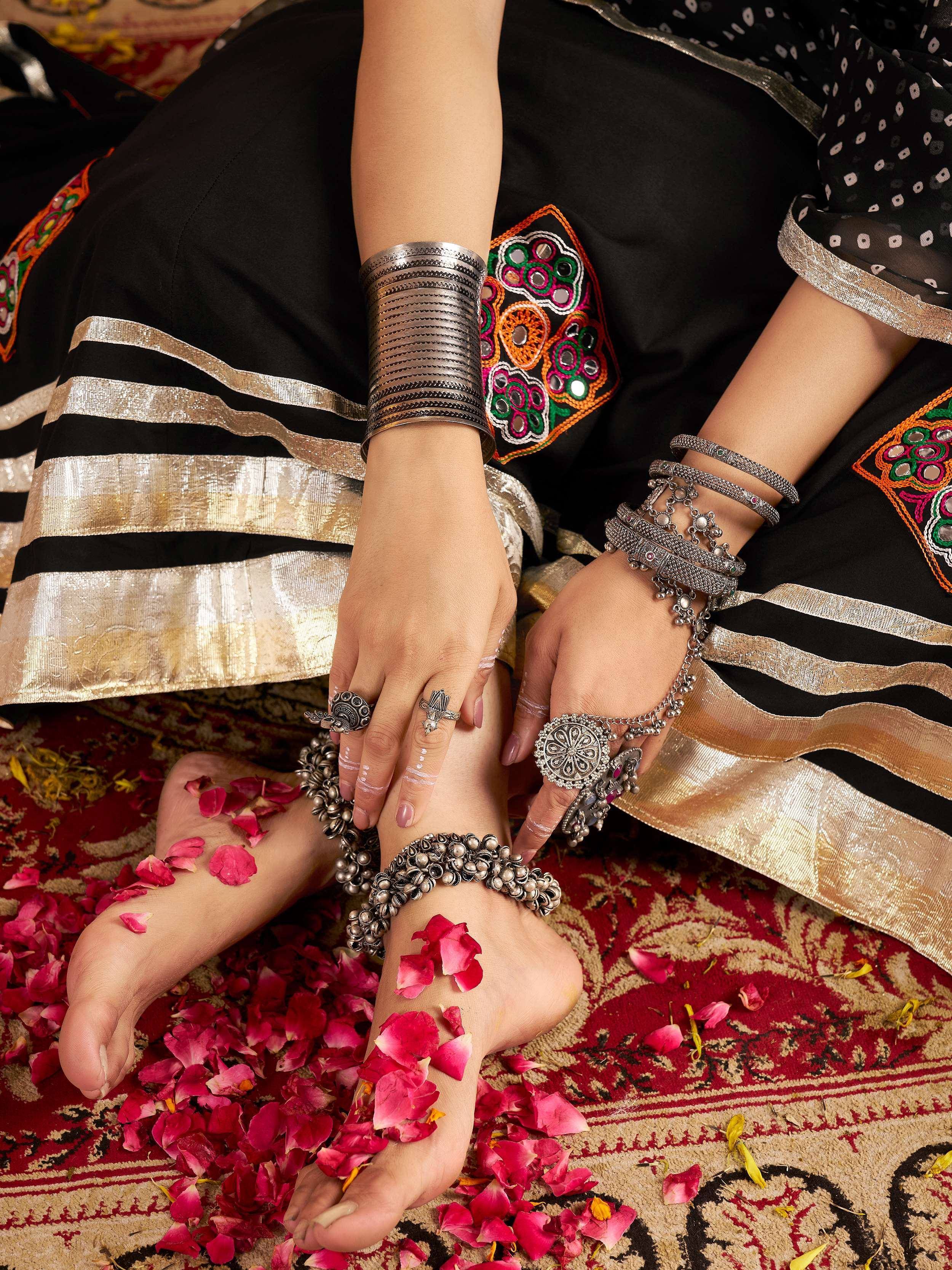 Black ethnic salwar kameez with mirror work, silver jewelry, and rose petals on rug
