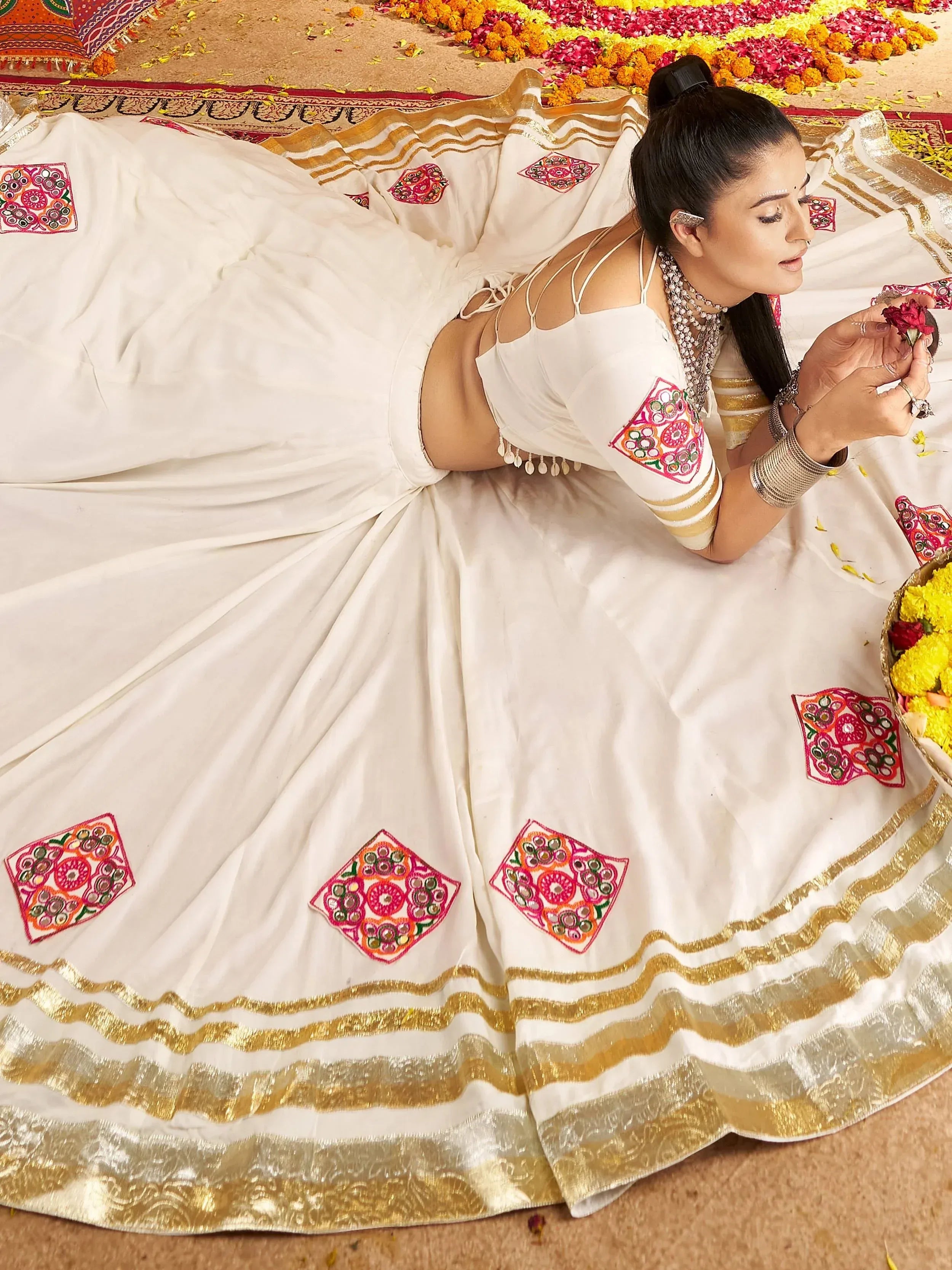 White ethnic lehenga with mirror work and gold trim, styled with traditional jewelry for festive occasions