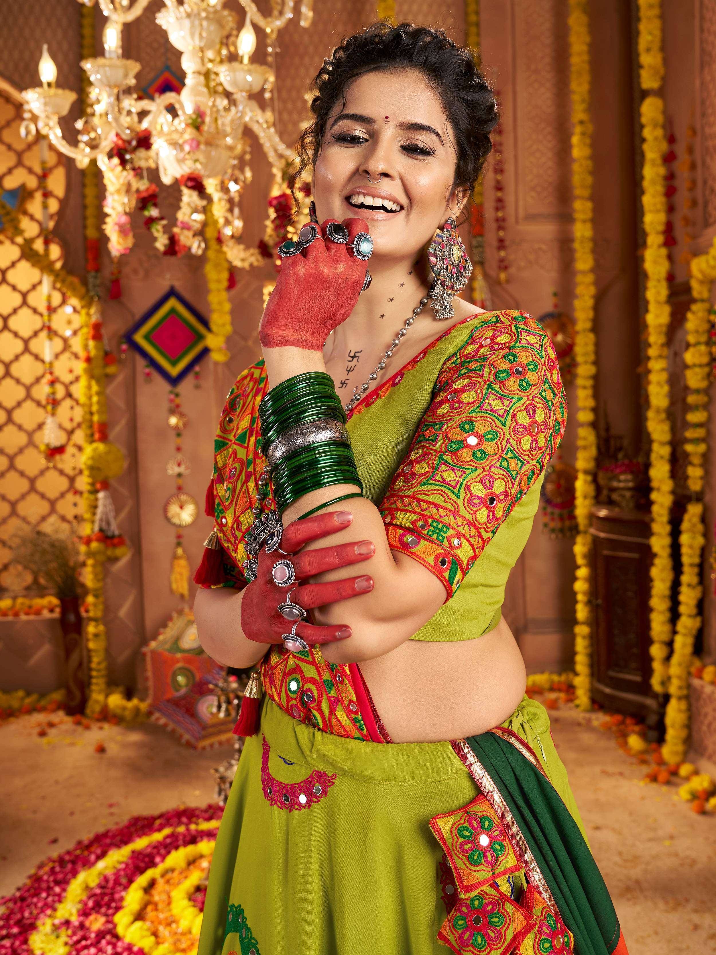 Woman in vibrant green embroidered lehenga choli with mirror work, traditional jewelry, and henna hands, festive Indian wedding decor