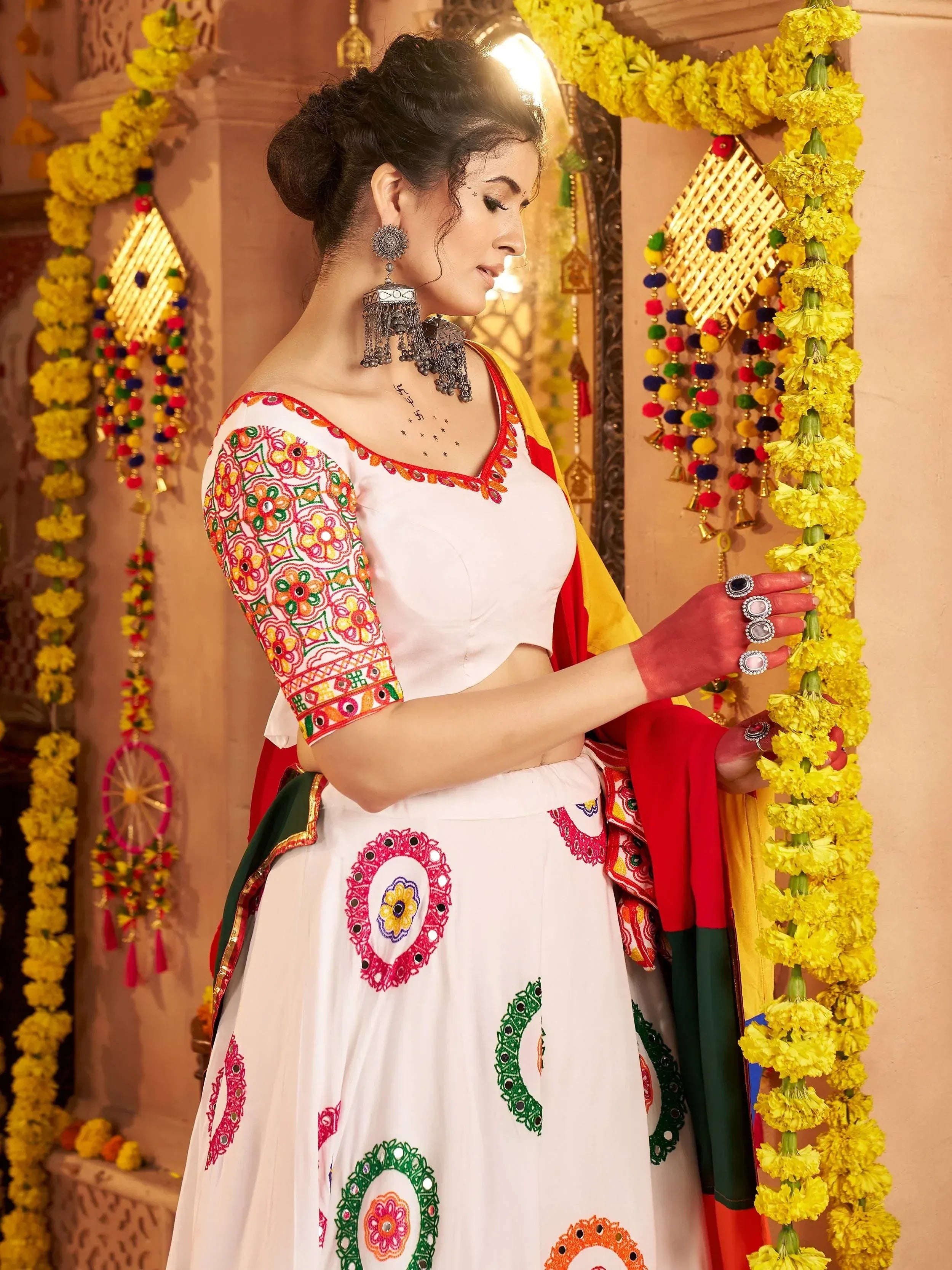 Woman in white embroidered lehenga choli with colorful floral patterns, traditional jewelry, and marigold garlands