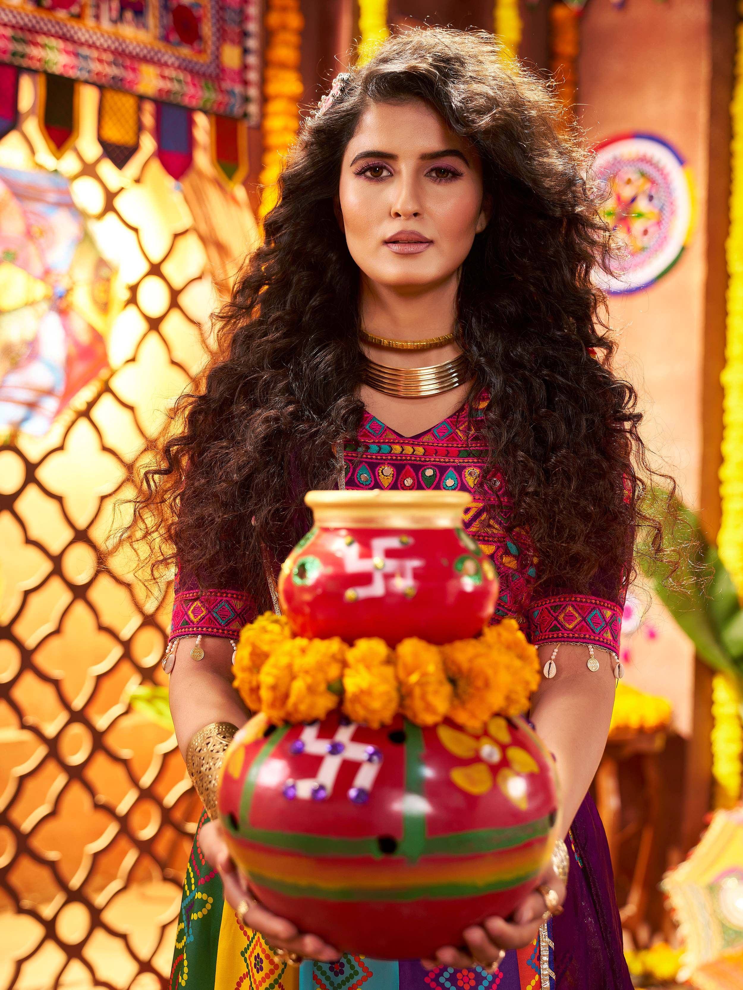Woman in colorful Indian ethnic wear holding decorative pots with marigolds, festive backdrop