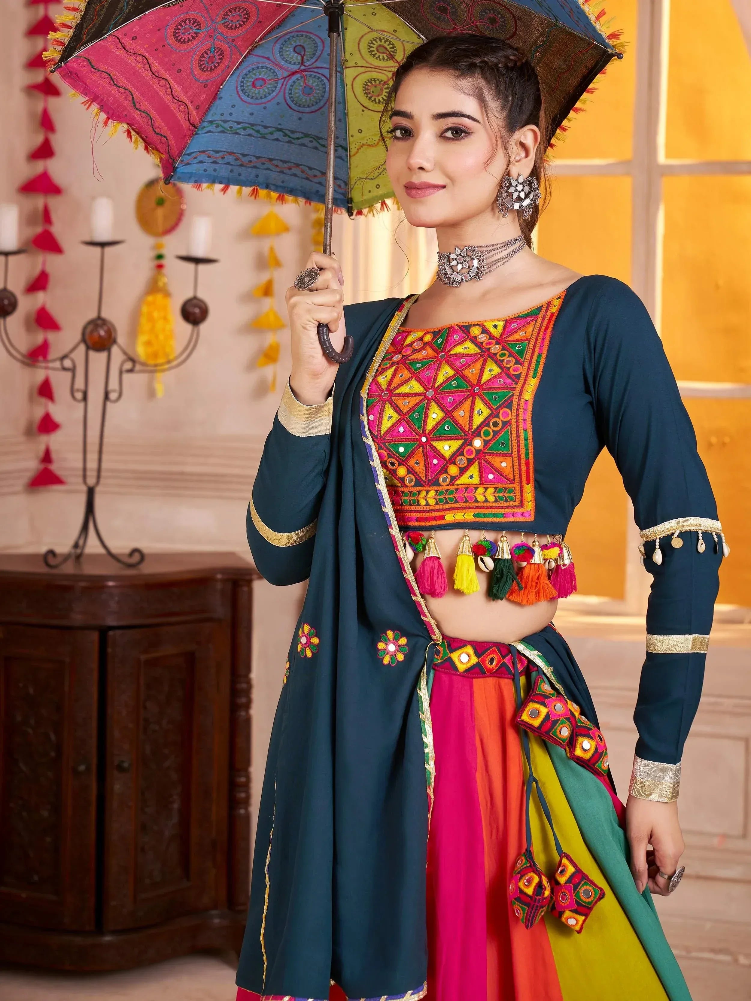Woman in colorful Indian ethnic wear with mirror work, holding patterned umbrella, traditional jewelry