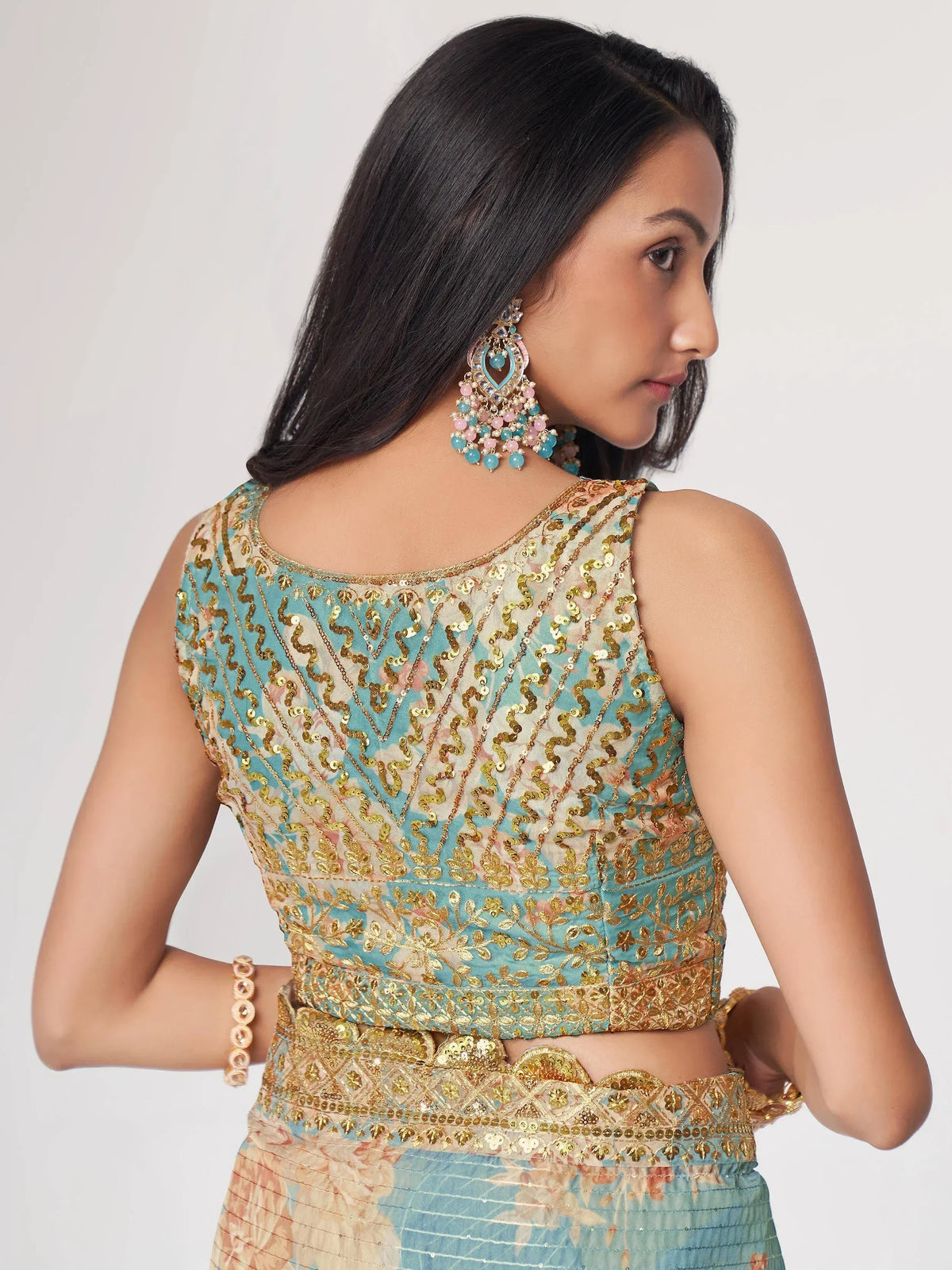 Woman in designer lehenga choli with gold sequin embroidery and matching earrings, showcasing ethnic Indian wear.