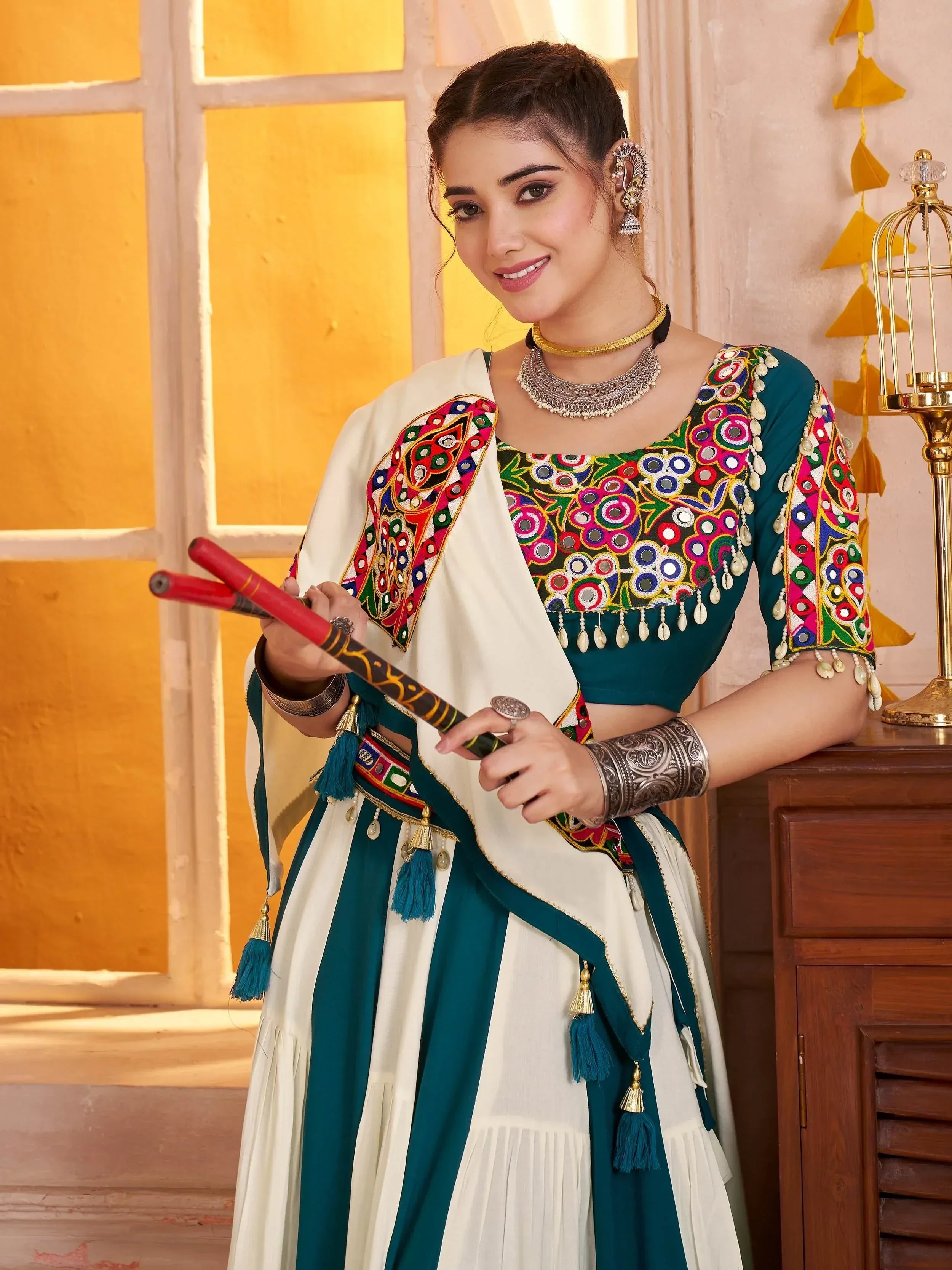 Woman in vibrant green and white embroidered ethnic wear with mirror work, holding traditional sticks, festive Indian attire