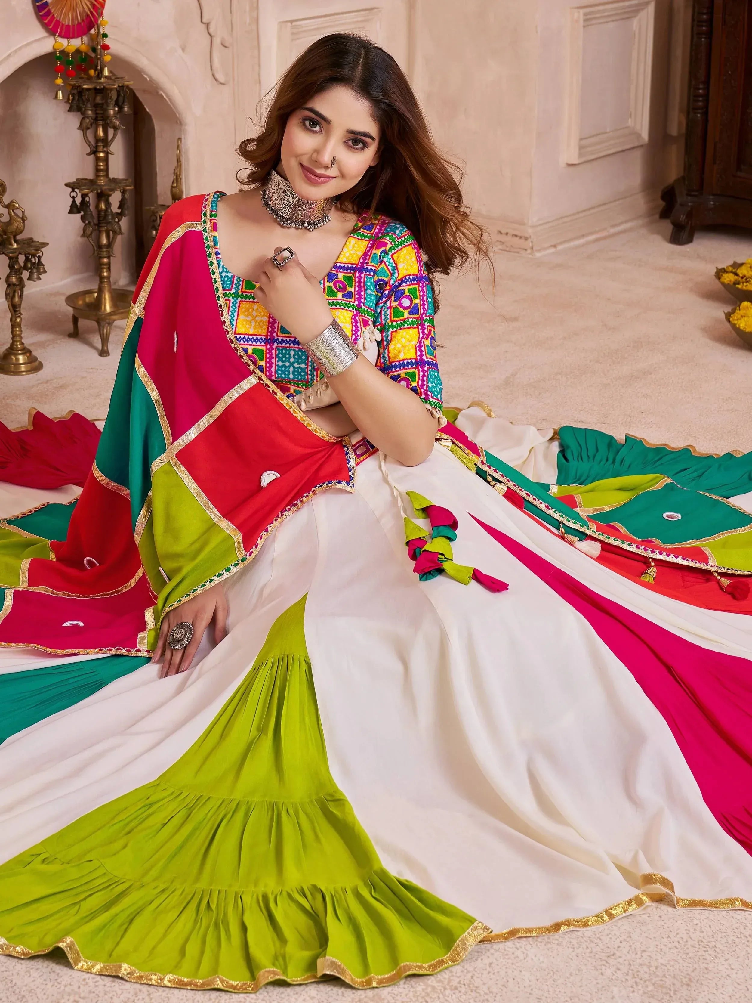 Woman in colorful Indian ethnic wear with embroidered top, white and green skirt, and vibrant dupatta, styled for festive occasions.