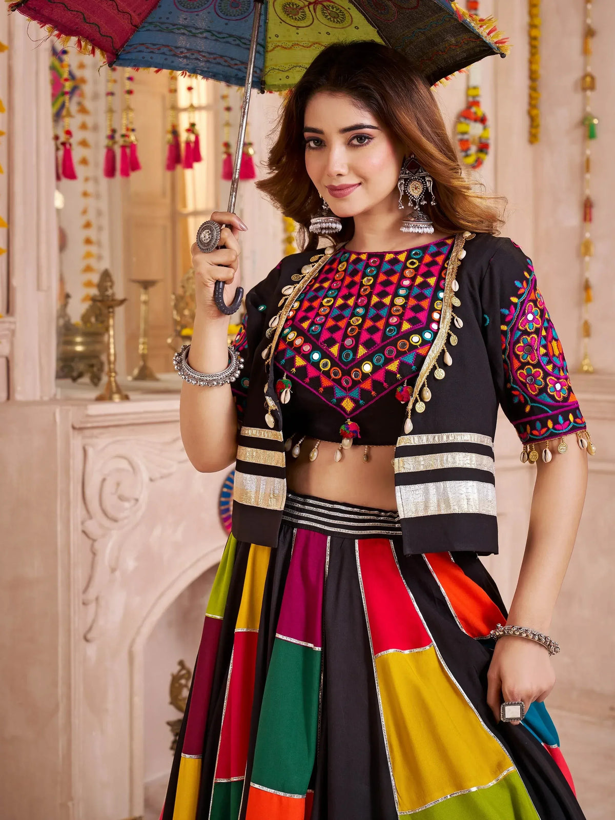 Woman in colorful Indian ethnic wear with mirror work blouse and patchwork lehenga, holding decorative umbrella