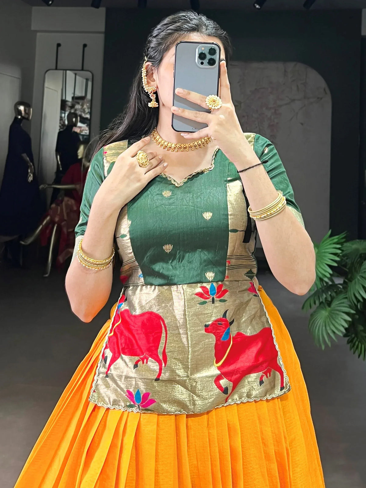Green and orange ethnic lehenga with red bull embroidery, gold jewelry, and floral accents