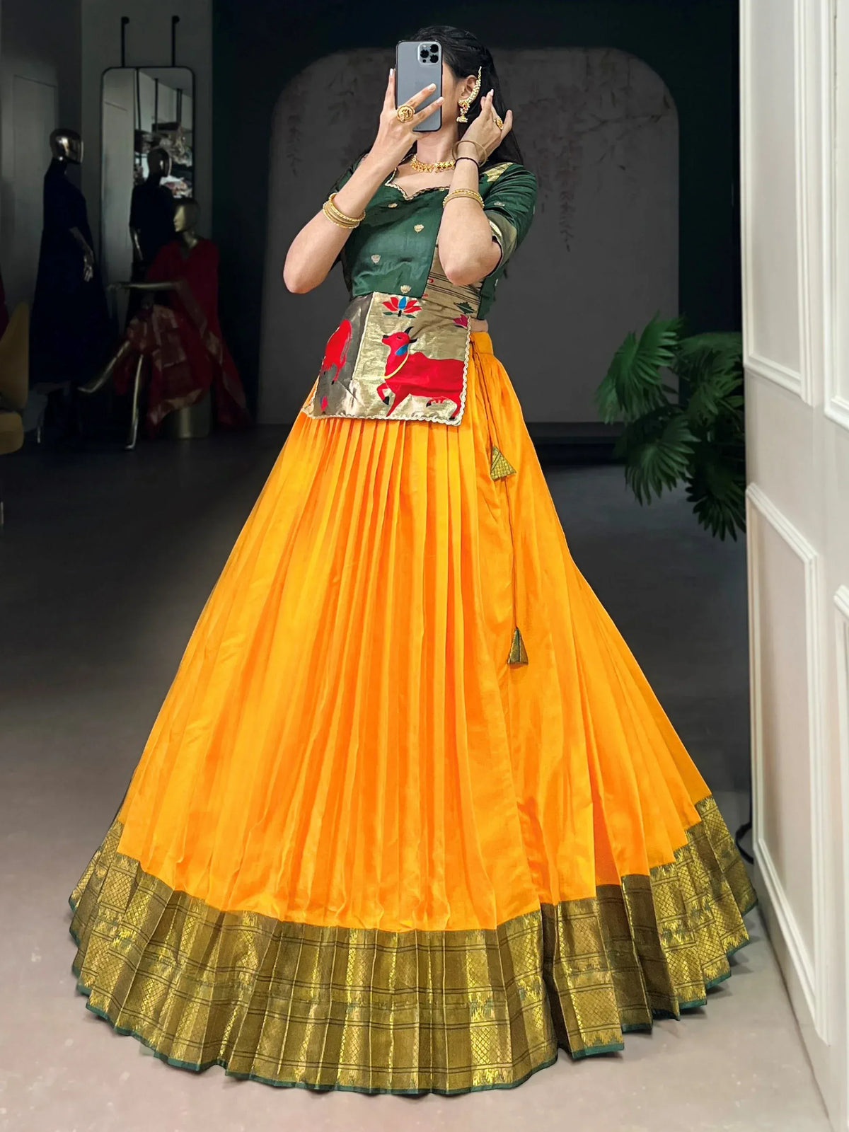 Vibrant orange pleated lehenga with golden border, green blouse, and embroidered waistband for Indian ethnic wear.