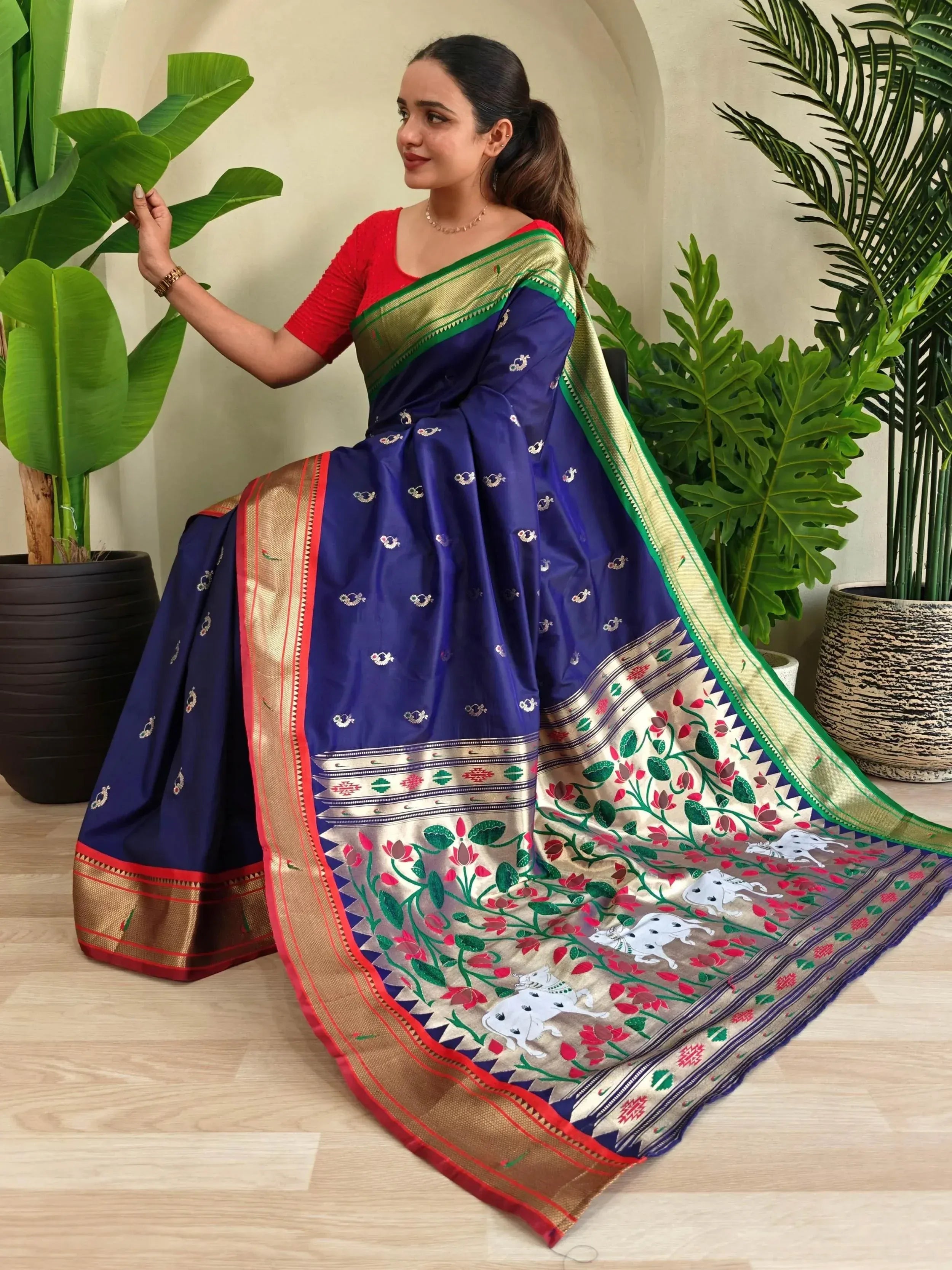 Woman in navy blue silk saree with floral and cow motifs, gold border, red blouse, ideal for Indian ethnic wear