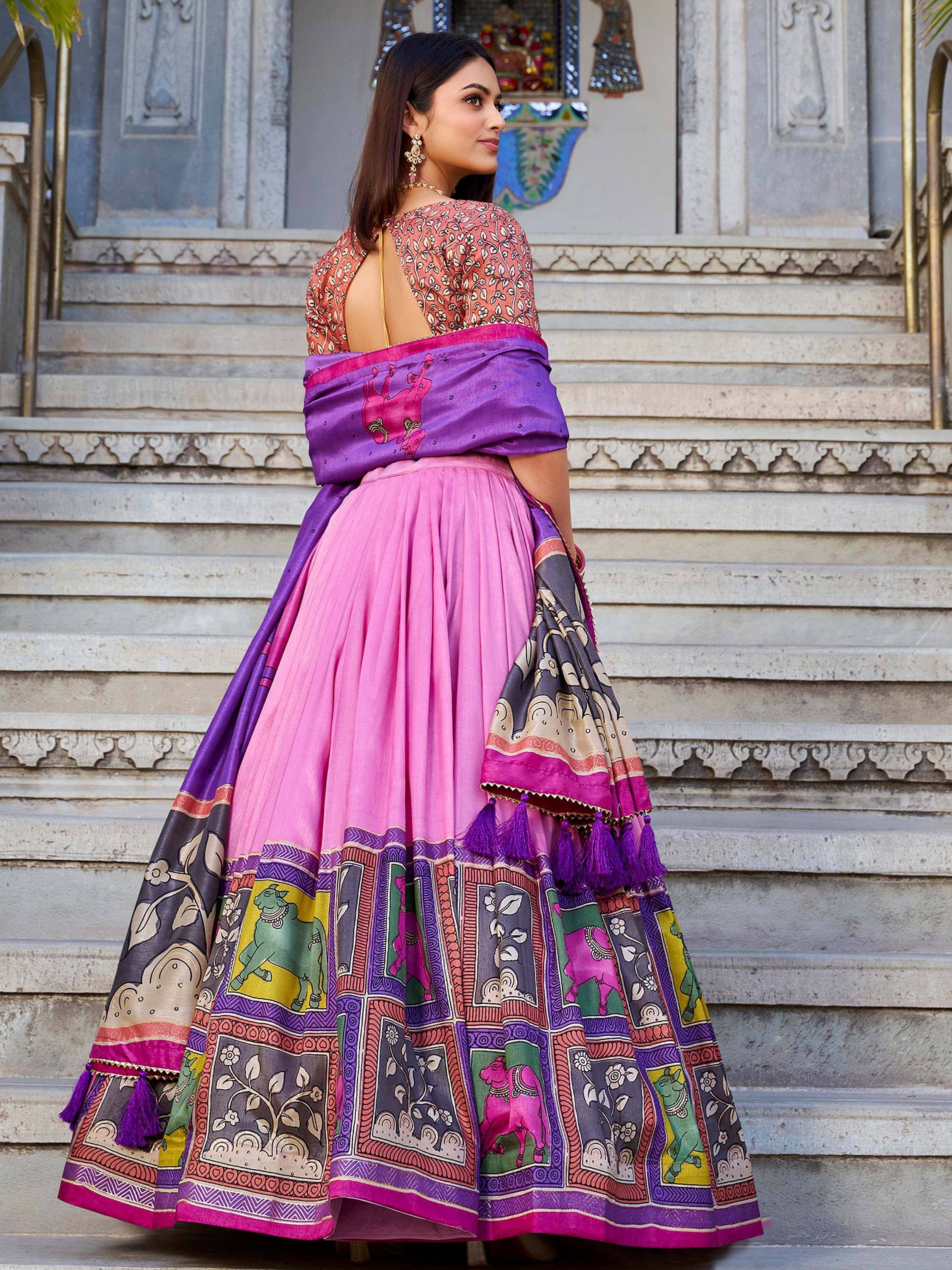 Woman in vibrant pink and purple printed lehenga choli with animal motifs, standing on stone steps