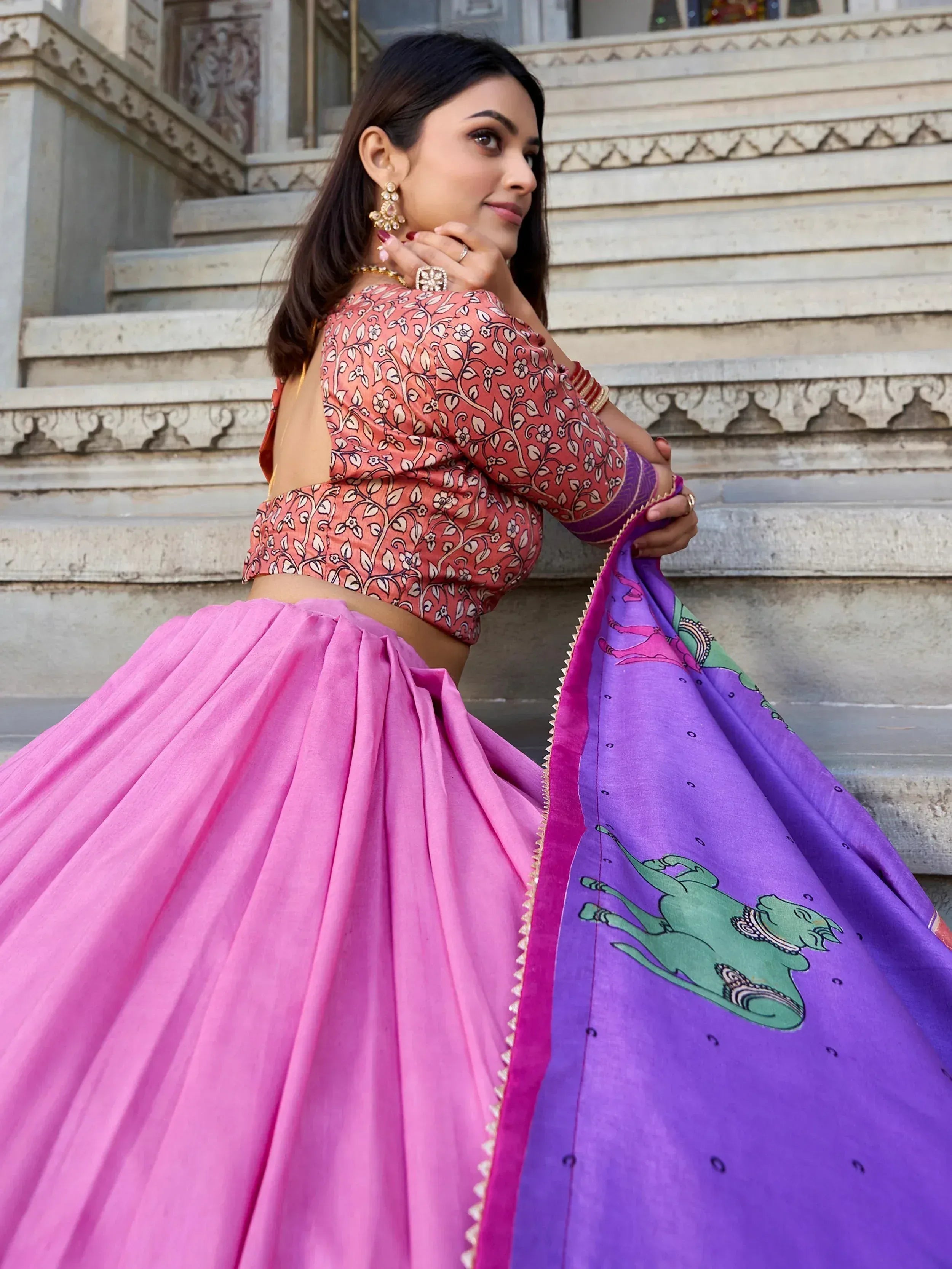 Woman in vibrant pink lehenga with floral blouse and purple dupatta featuring green horse print, styled for Indian ethnic wear.