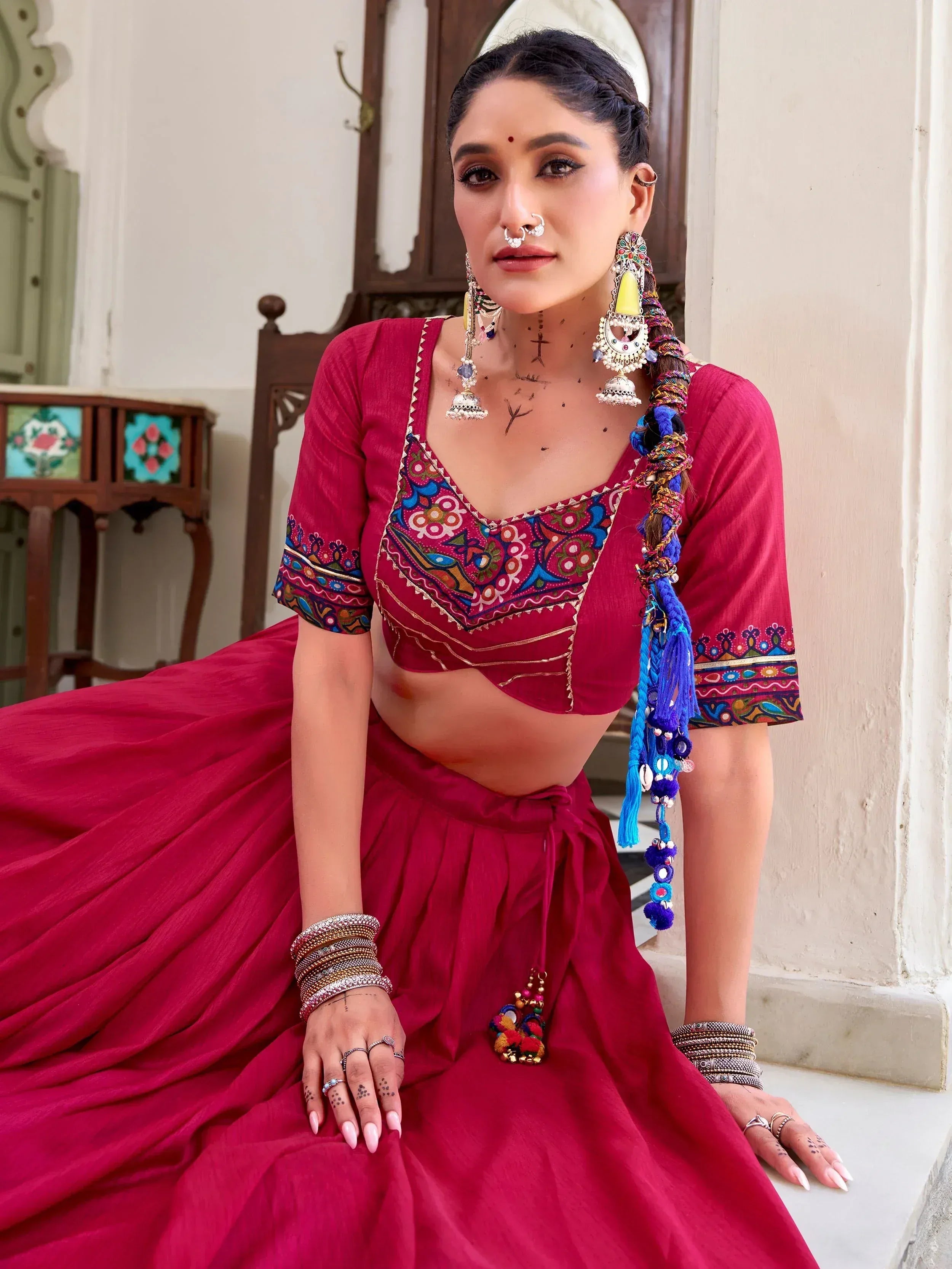 Woman in vibrant red ethnic lehenga choli with colorful embroidery, traditional jewelry, and braided hair