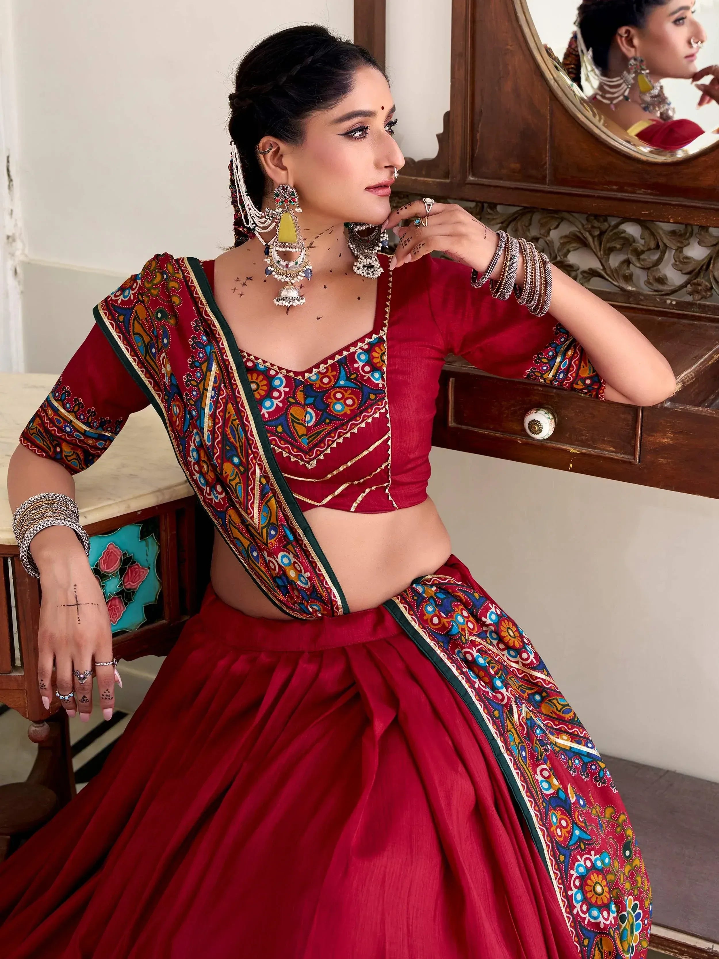 Woman in red ethnic lehenga choli with colorful printed dupatta, traditional jewelry, and mirror reflection