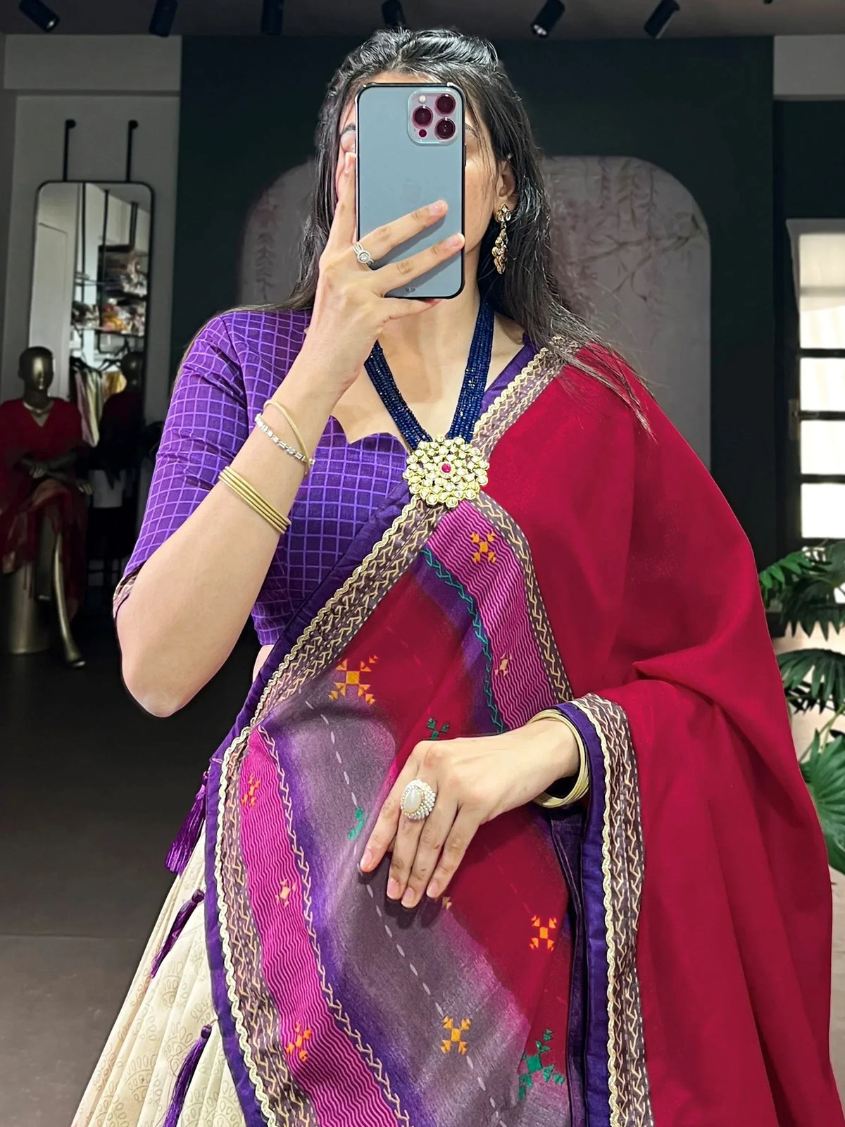 Vibrant purple and red ethnic saree with intricate embroidery and gold border, paired with designer jewelry.