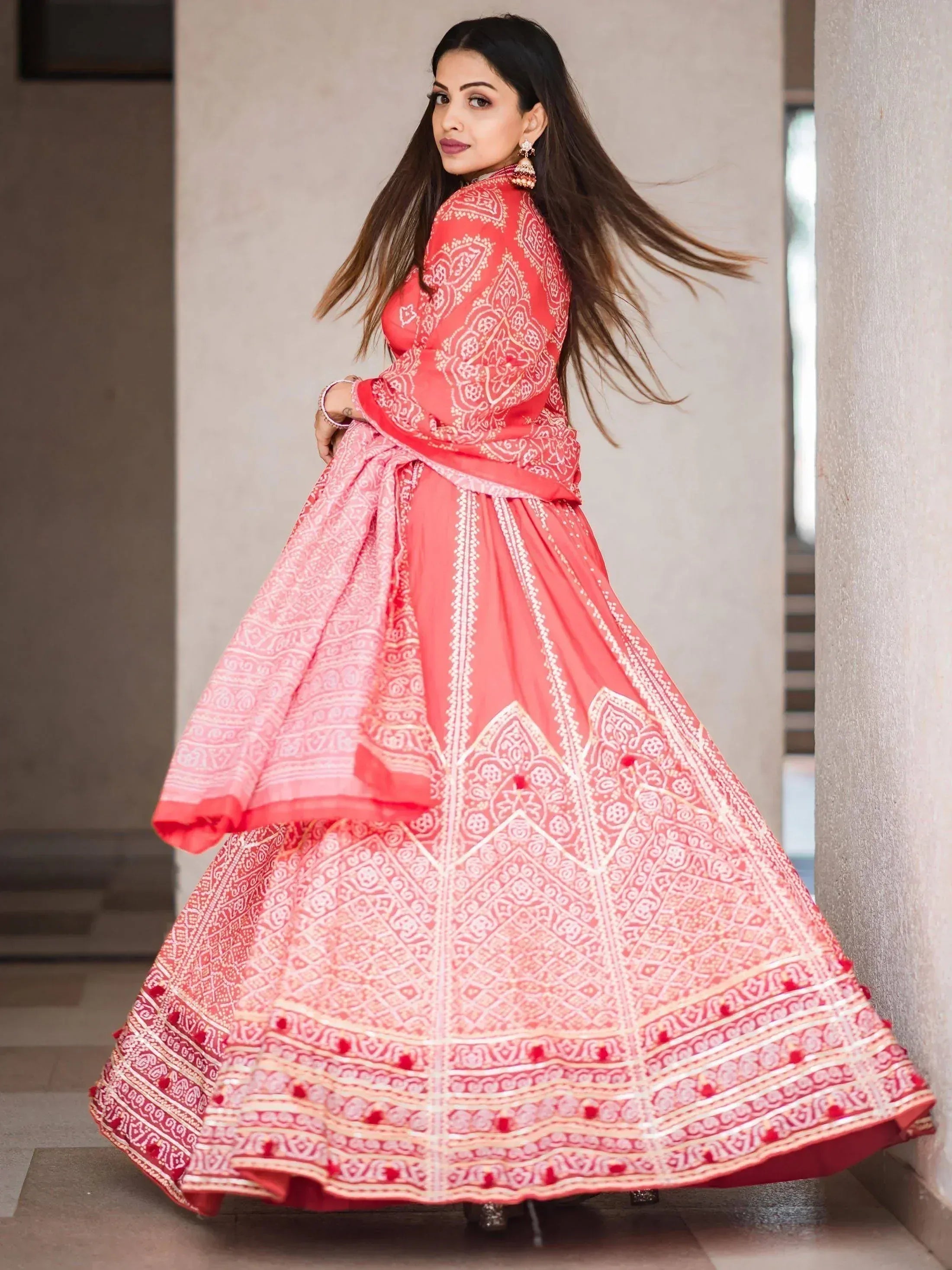 Coral pink printed lehenga choli with intricate white patterns and pom-pom detailing, perfect for Indian ethnic occasions.