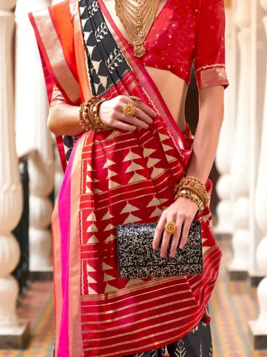 Red and black ethnic saree with geometric print, gold jewelry, and clutch for Indian occasions