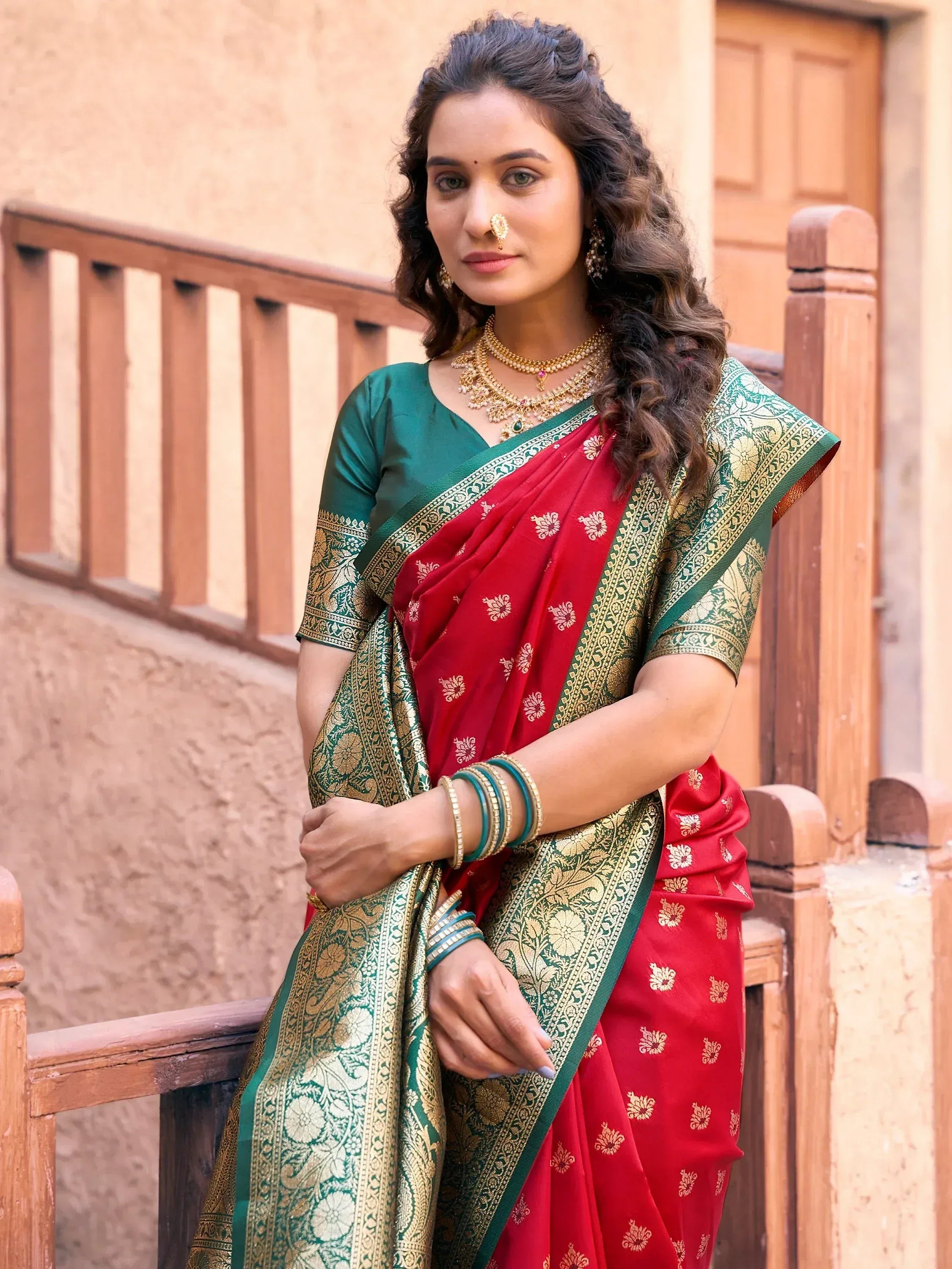 Red and green designer saree with gold embroidery, paired with matching blouse and traditional jewelry