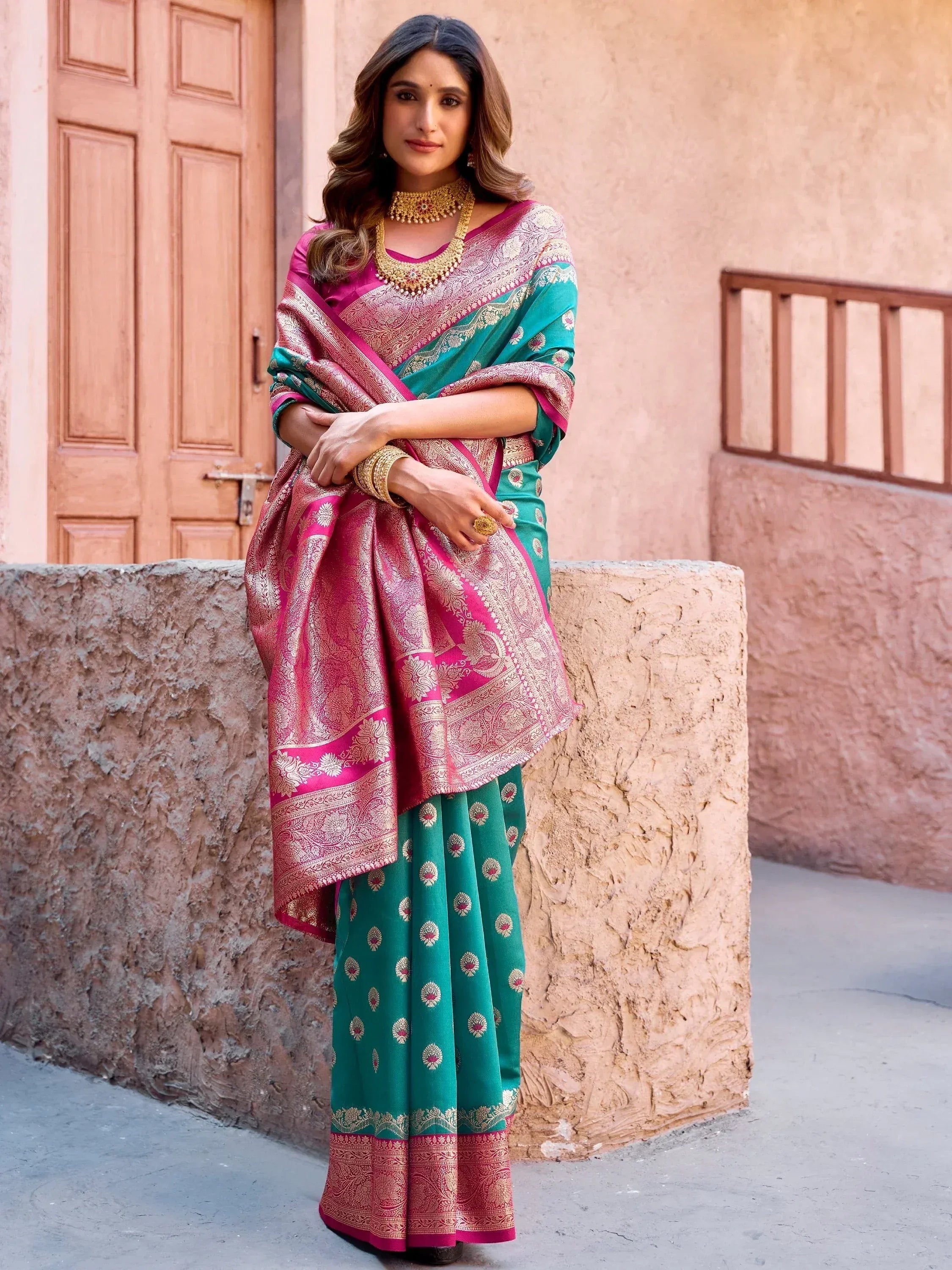 Elegant woman in designer saree with pink and green hues, adorned with gold jewelry, perfect for ethnic occasions.