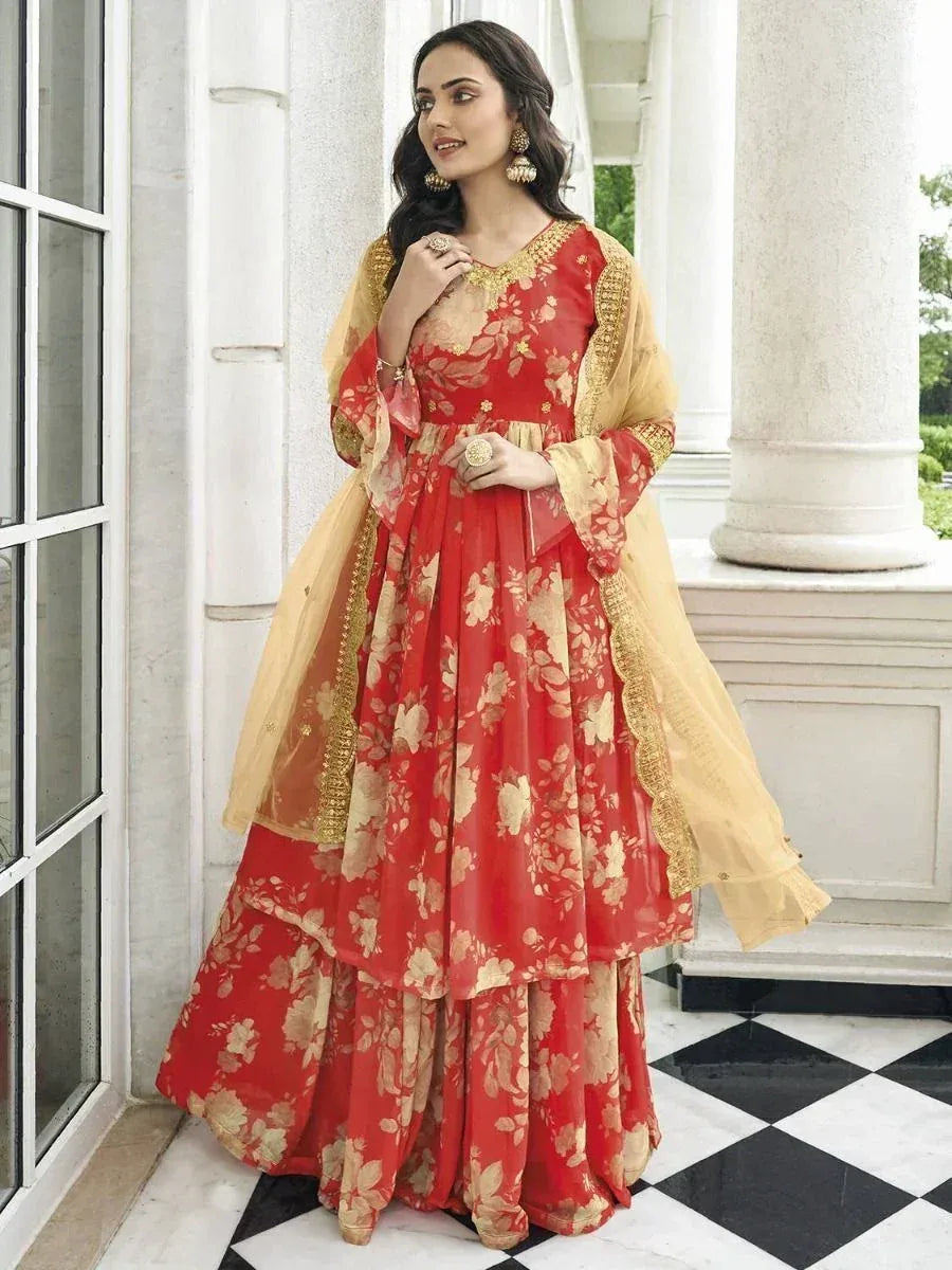 Woman in red floral printed ethnic gown with yellow dupatta, traditional jewelry, outdoor setting