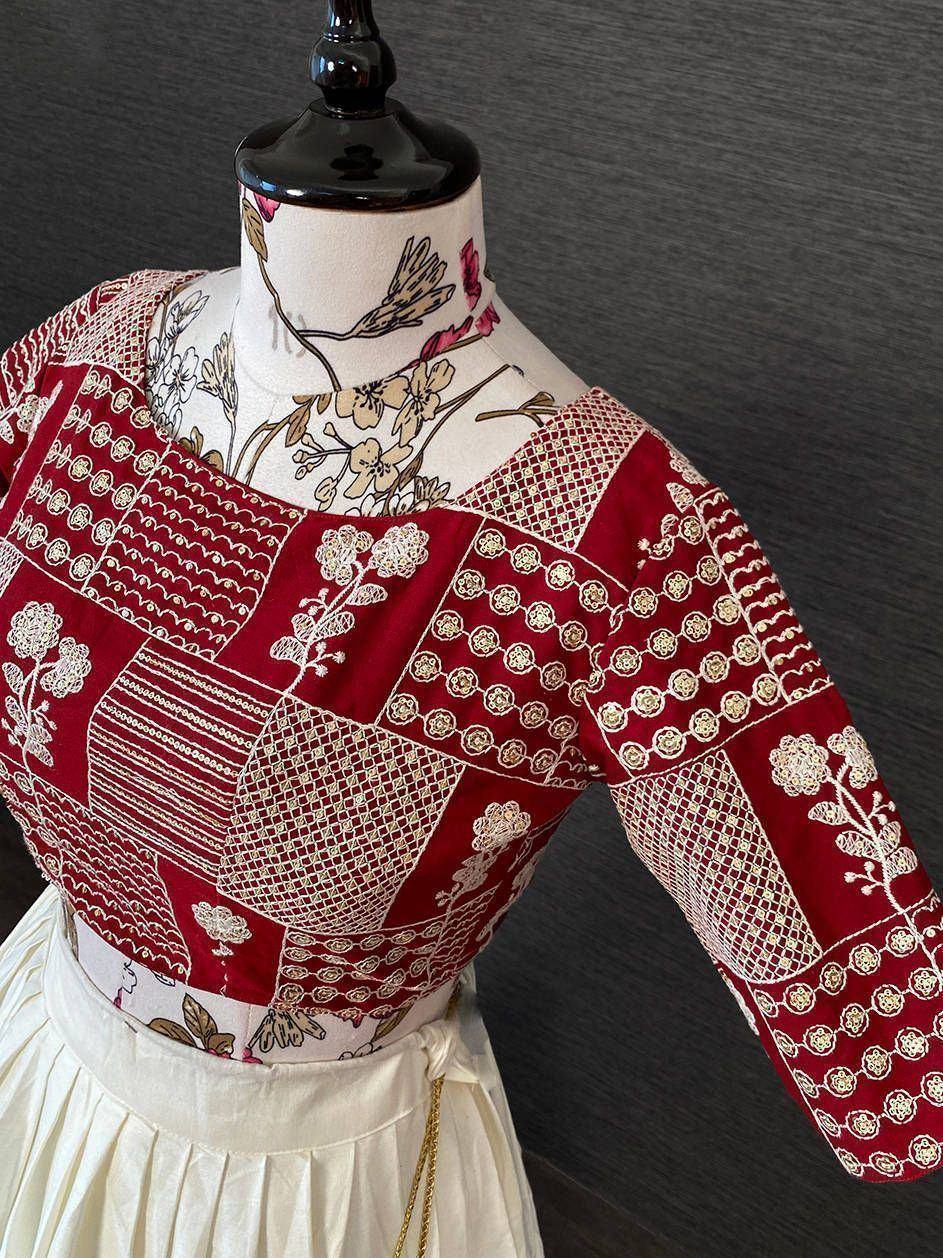 Red embroidered blouse with patchwork design, floral motifs, and gold detailing on mannequin