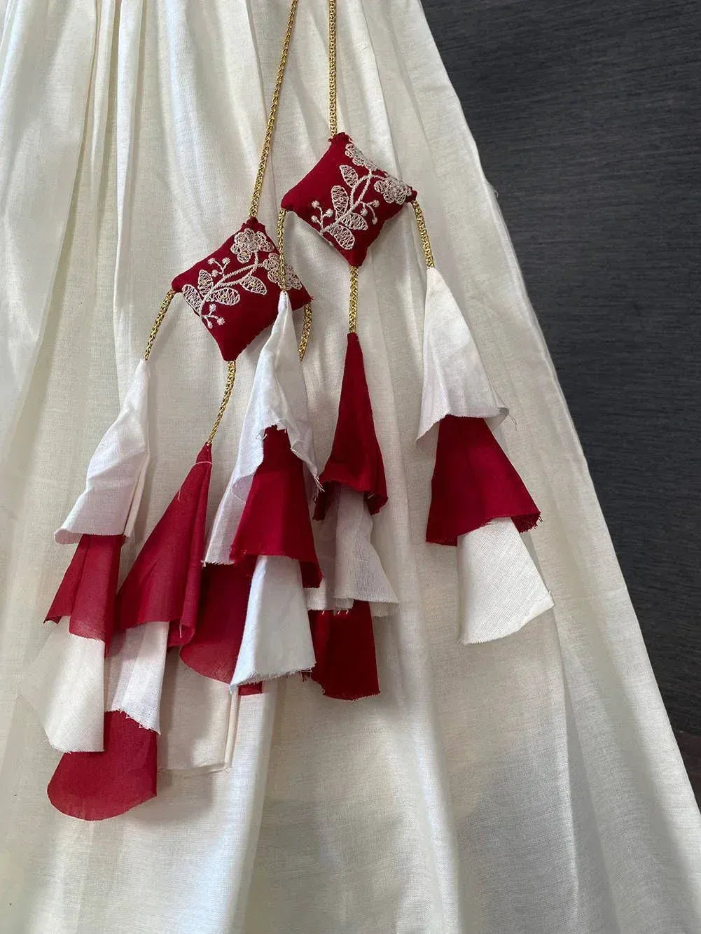 White ethnic gown with red embroidered tassels and layered ruffles, perfect for Indian festive wear