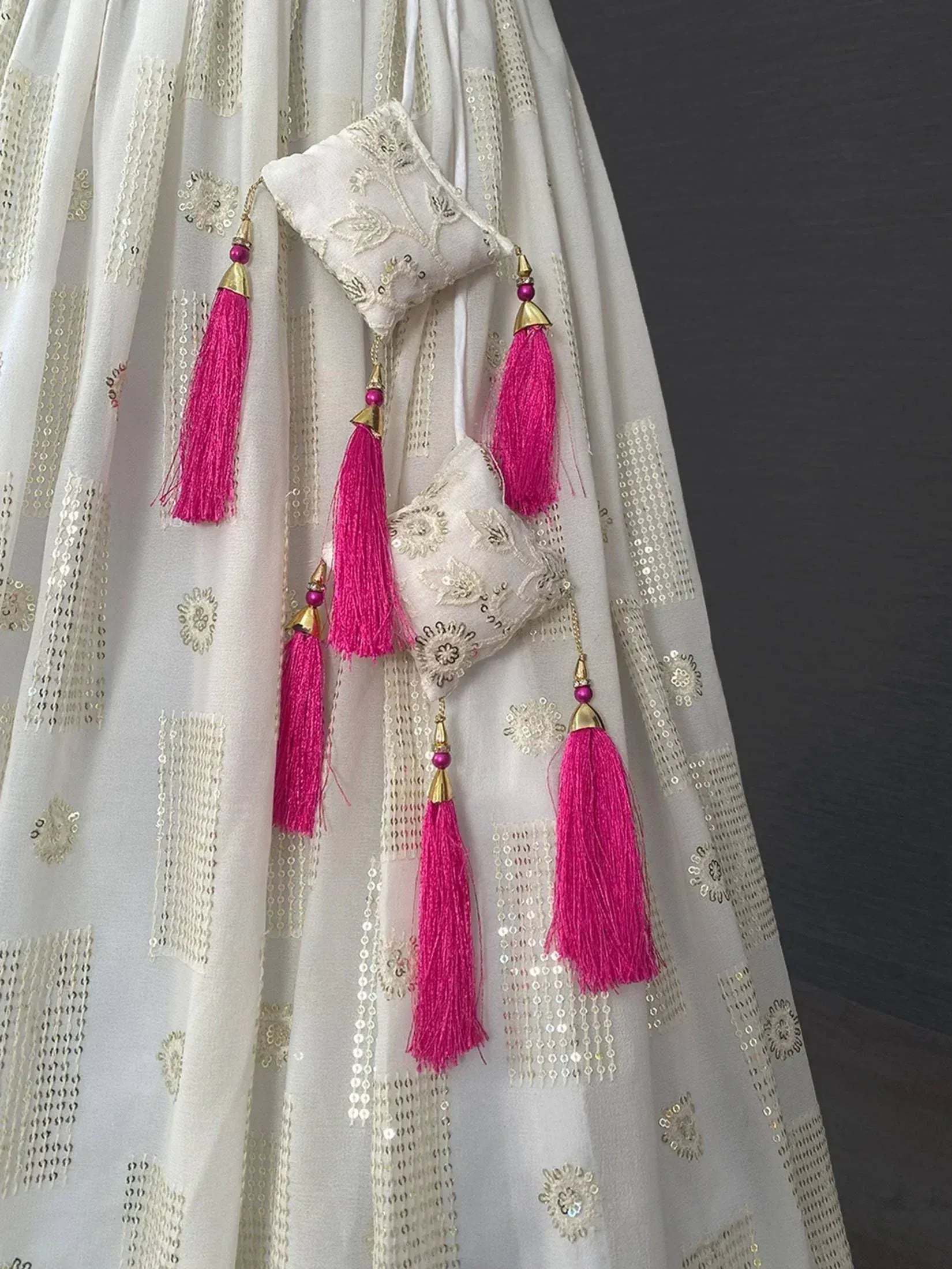 White ethnic gown with gold sequin embroidery and pink tassels, perfect for Indian festive wear.