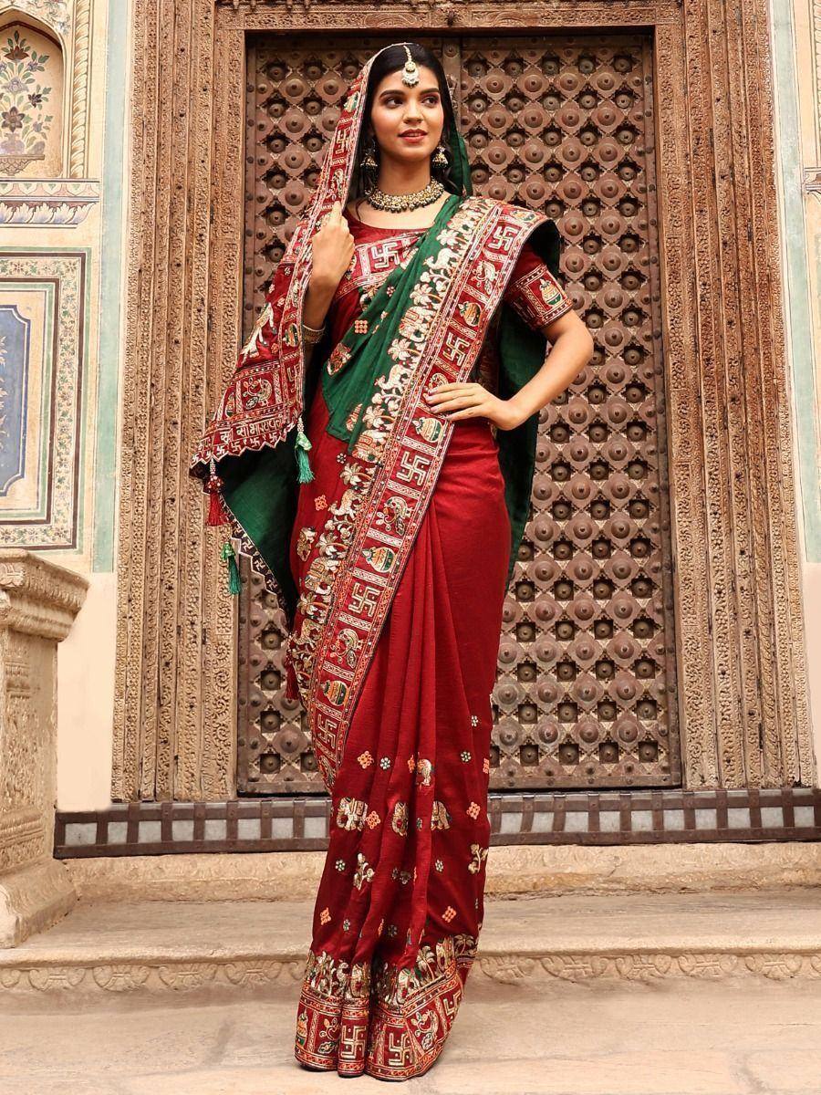 Red and green embroidered saree with traditional Indian motifs, styled with jewelry against ornate door