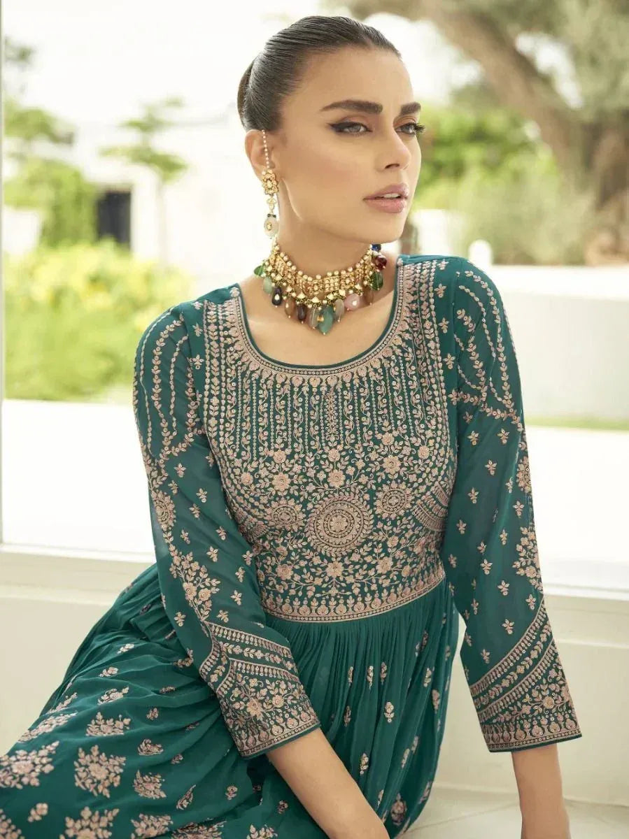 Woman wearing an emerald green embroidered ethnic gown with gold jewelry, sitting indoors