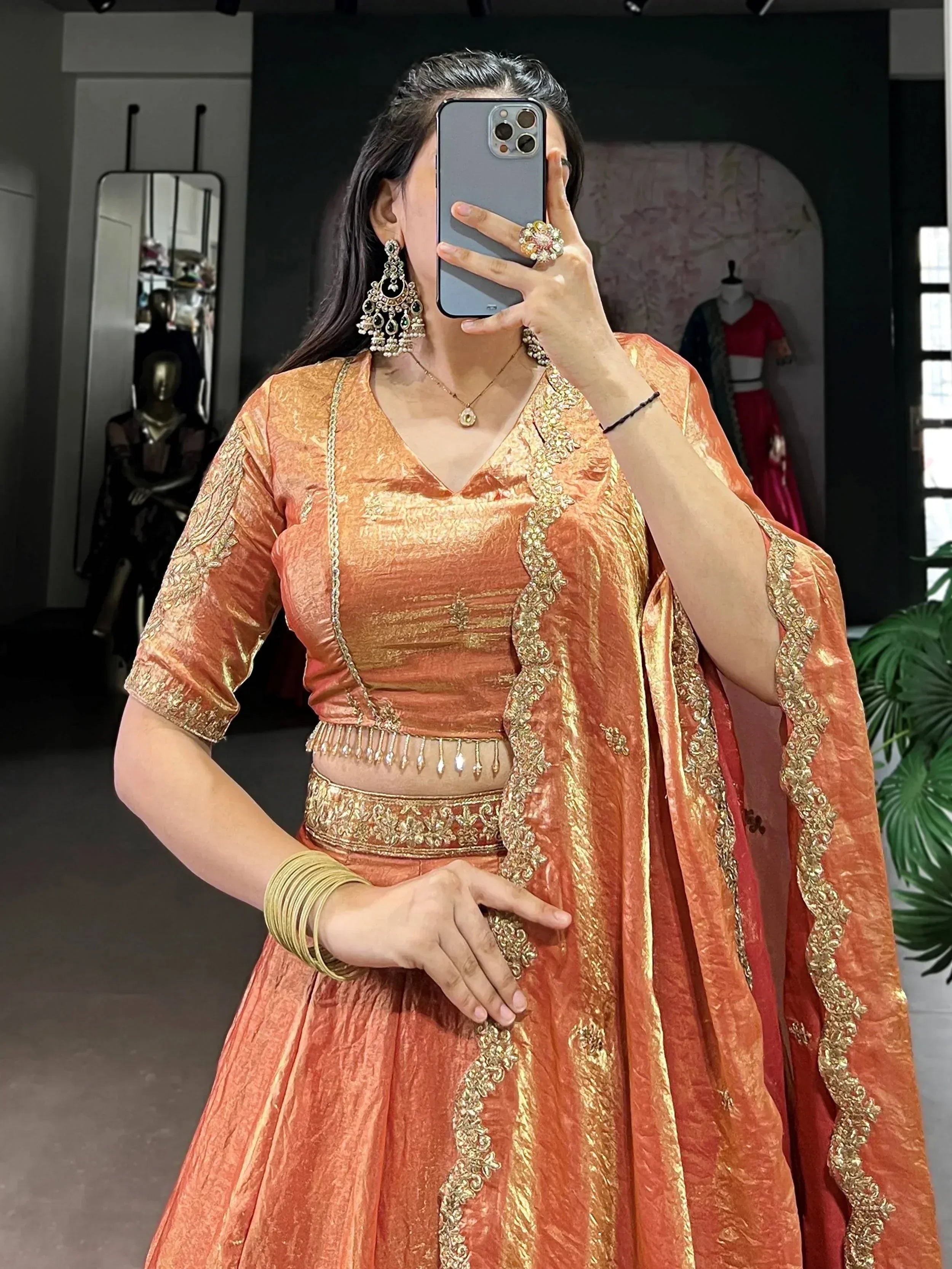 Woman in orange-gold designer lehenga choli with intricate embroidery and traditional jewelry