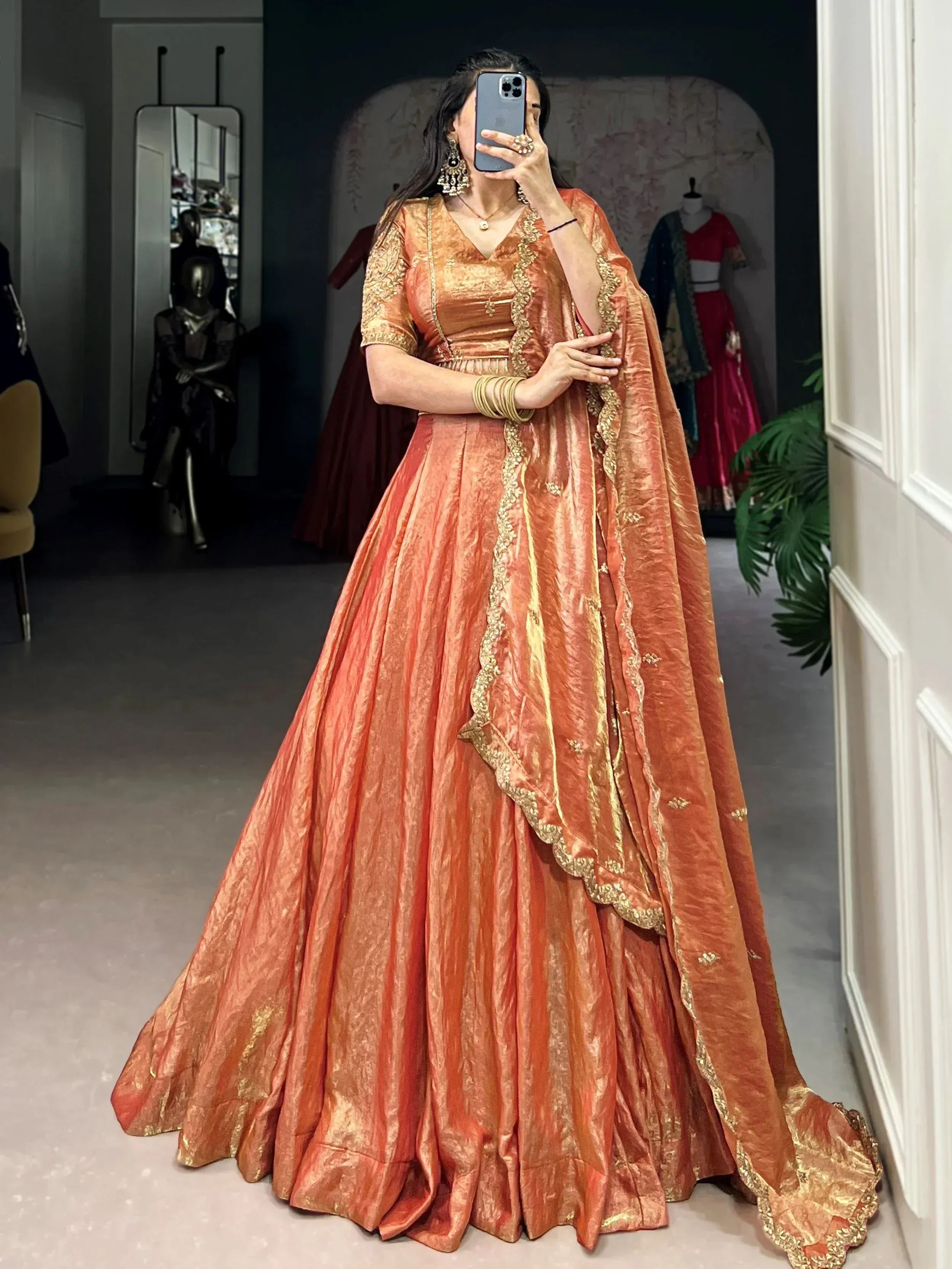 Woman in orange-gold designer lehenga choli with intricate embroidery, perfect for Indian ethnic wear occasions.