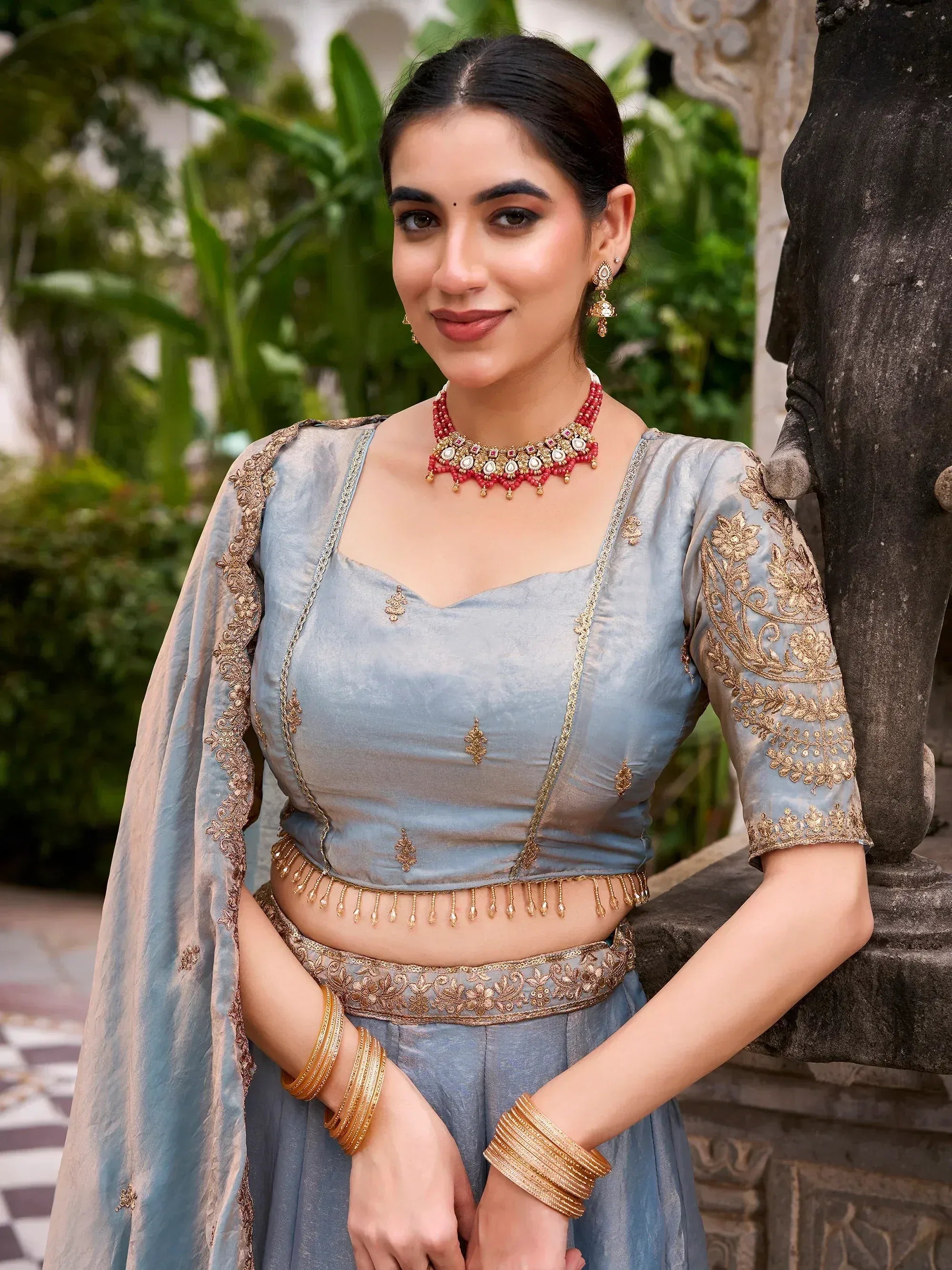 Woman in elegant blue designer lehenga choli with gold embroidery and red jewelry, perfect for Indian ethnic wear.
