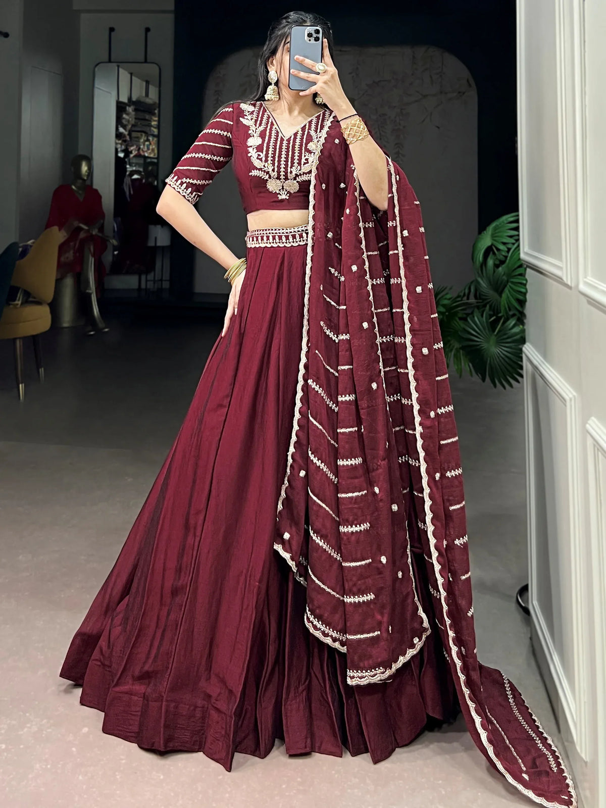 Woman wearing a maroon designer lehenga choli with gold embroidery and matching dupatta.
