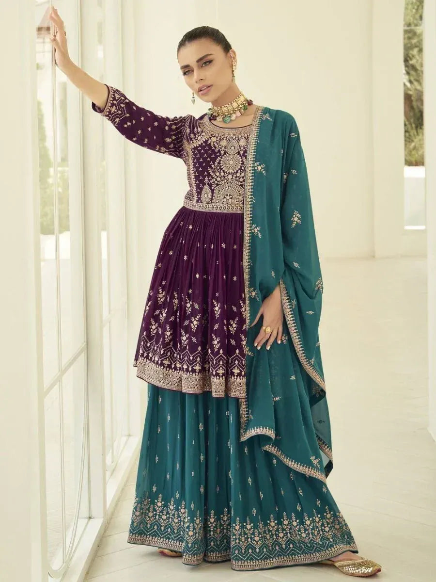 Woman in embroidered purple and teal ethnic suit with dupatta, standing indoors