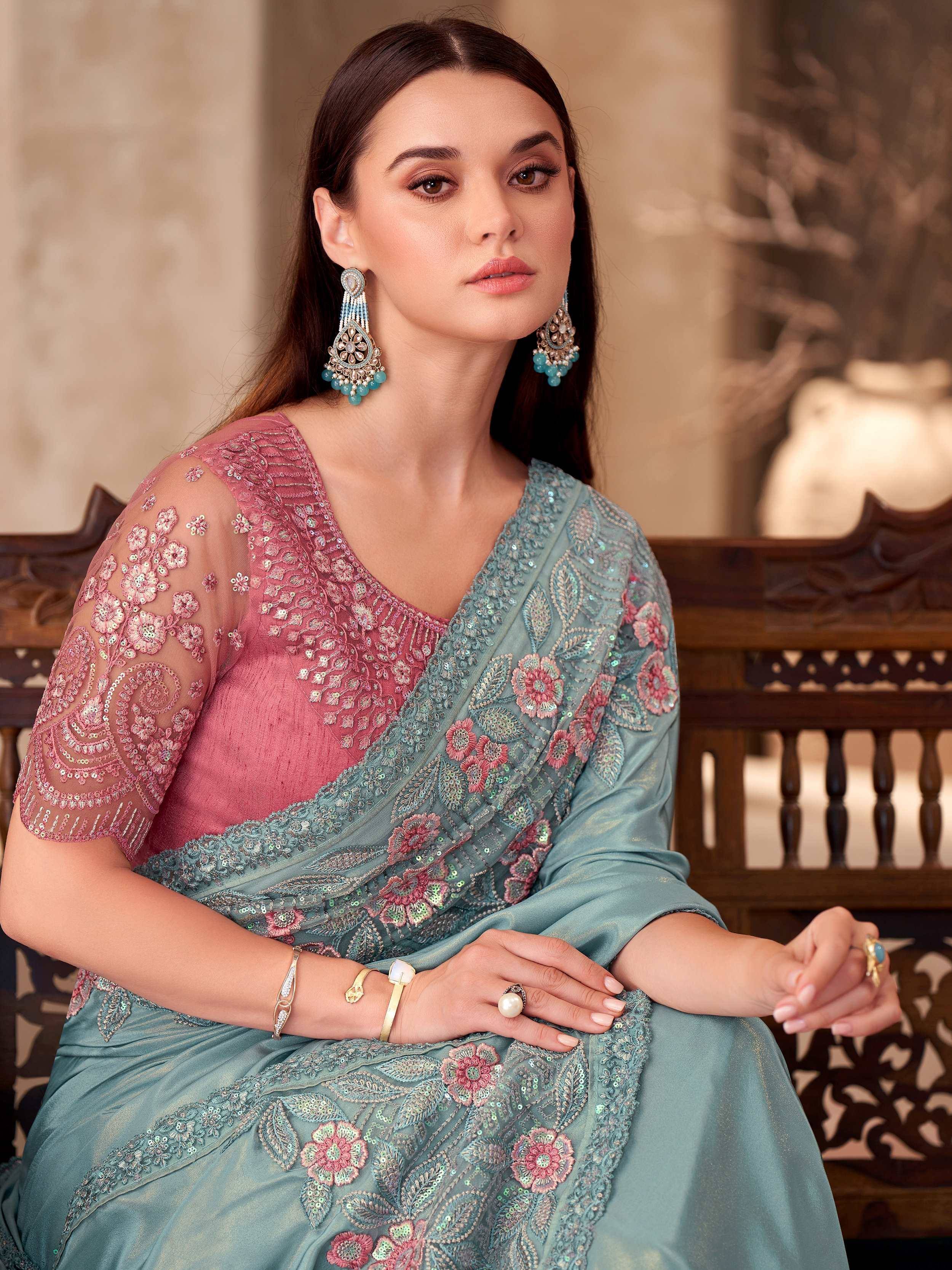 Elegant teal saree with pink floral embroidery and sequin work, paired with statement earrings for Indian ethnic wear.