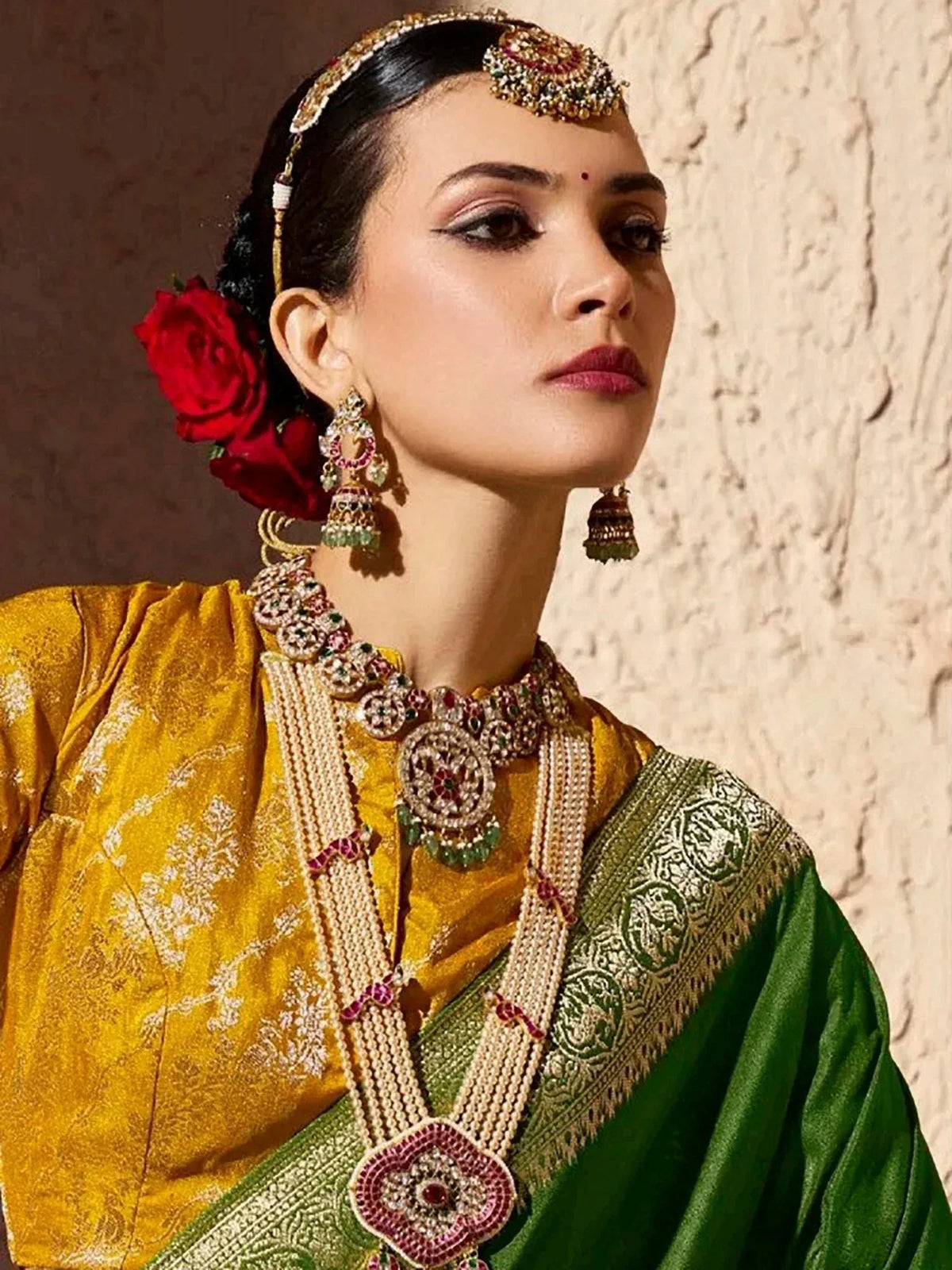 Elegant woman in yellow and green ethnic saree with intricate jewelry and red rose hair accessory